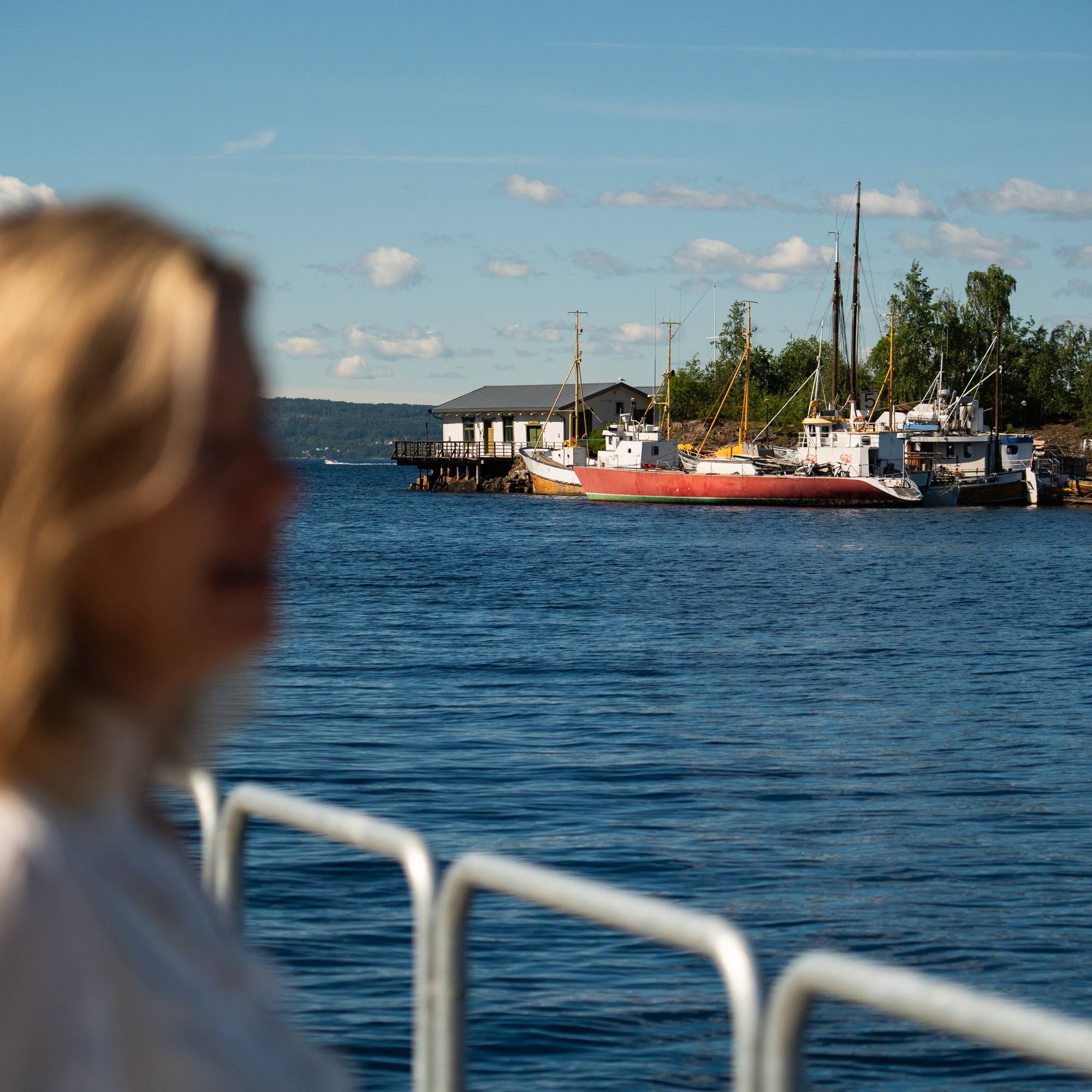 Blond kvinne i forgrunnen, øy med fortøyde båter bak
