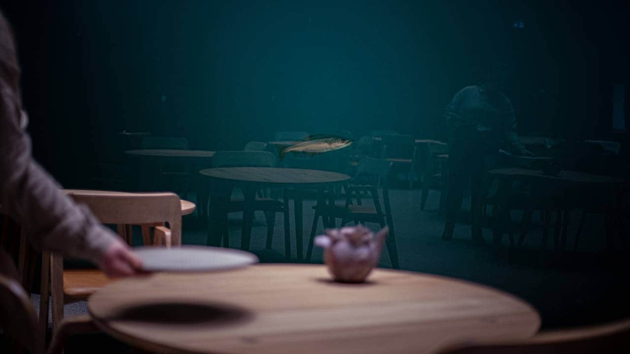 En enslig lyr svømmer utenfor vinduet på undervannsrestauranten Under. I forgrunnen ses en hånd som dekker på bordet.