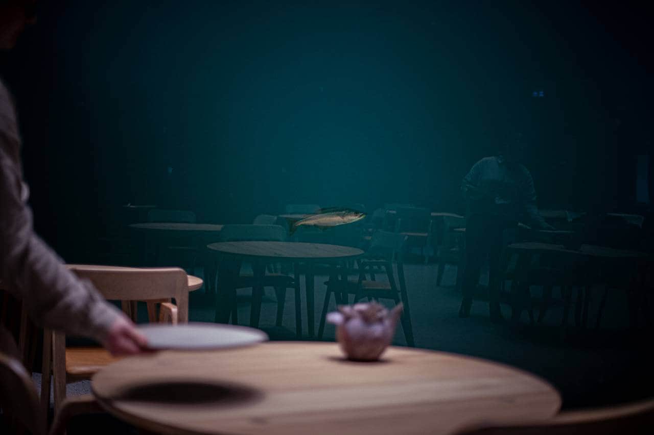 En enslig lyr svømmer utenfor vinduet på undervannsrestauranten Under. I forgrunnen ses en hånd som dekker på bordet.