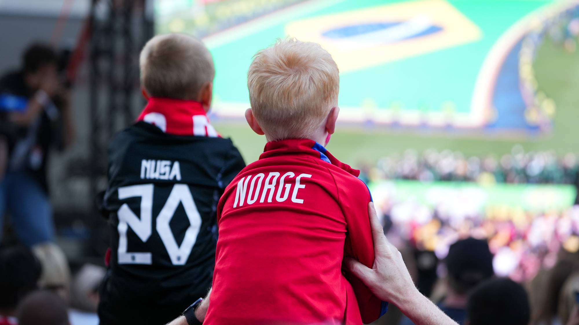 To barn som ser på fotball kamp. De begge har på seg fotball trøye