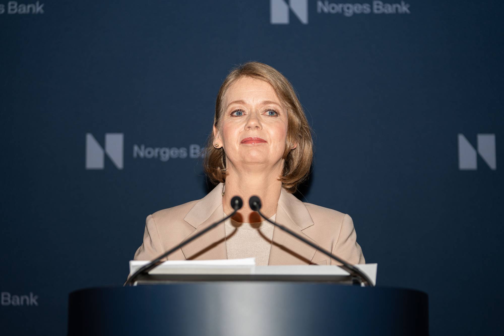 Ida Wolden Bache fotografert på en talerstol. Foran henne er mikrofoner, hun har på seg beige blazer