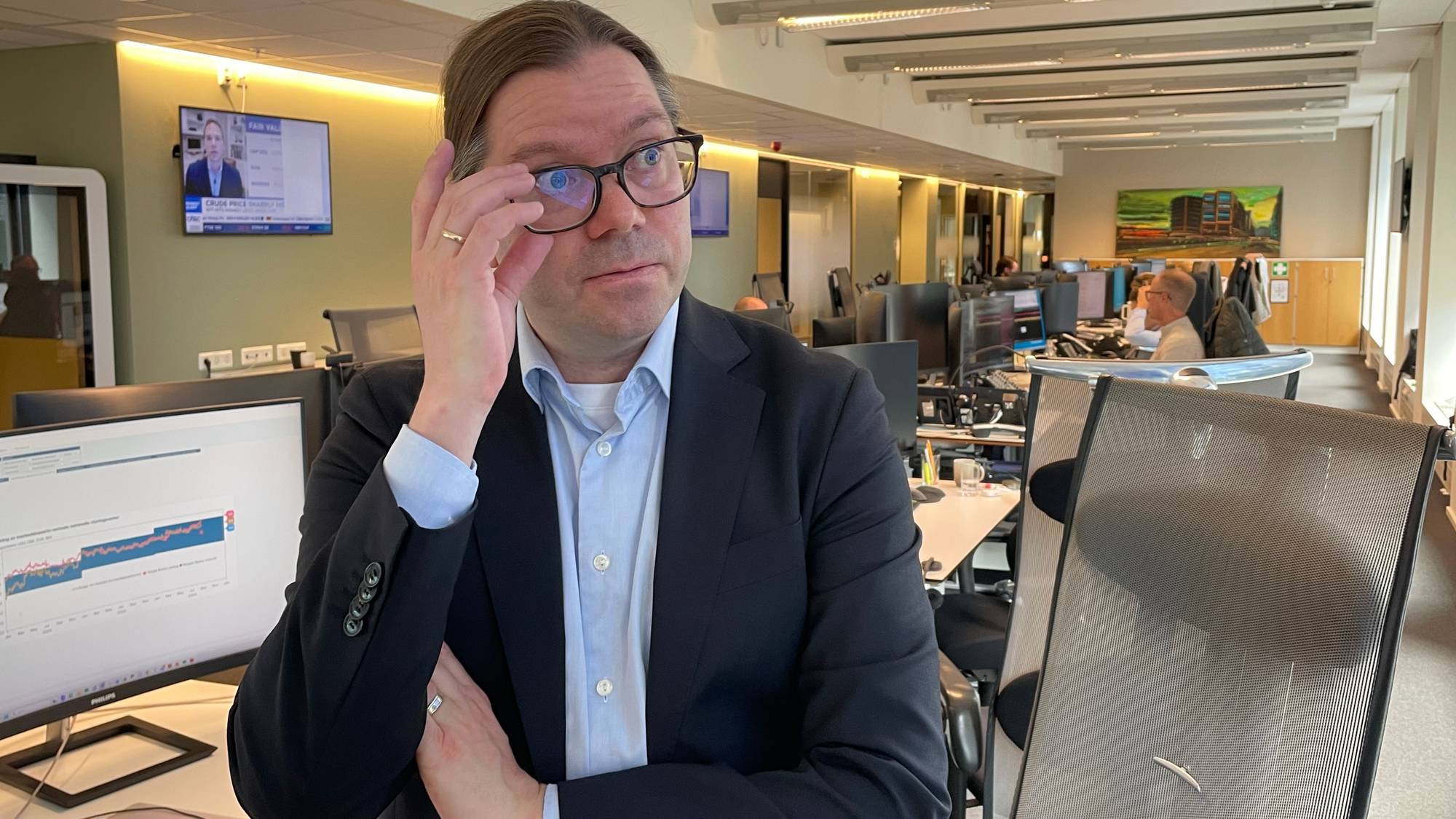 Handelsbankens sjeføkonom Marius Gonsholt Hov står i dressjakke og blå skjorte foran arbeidspulten sin