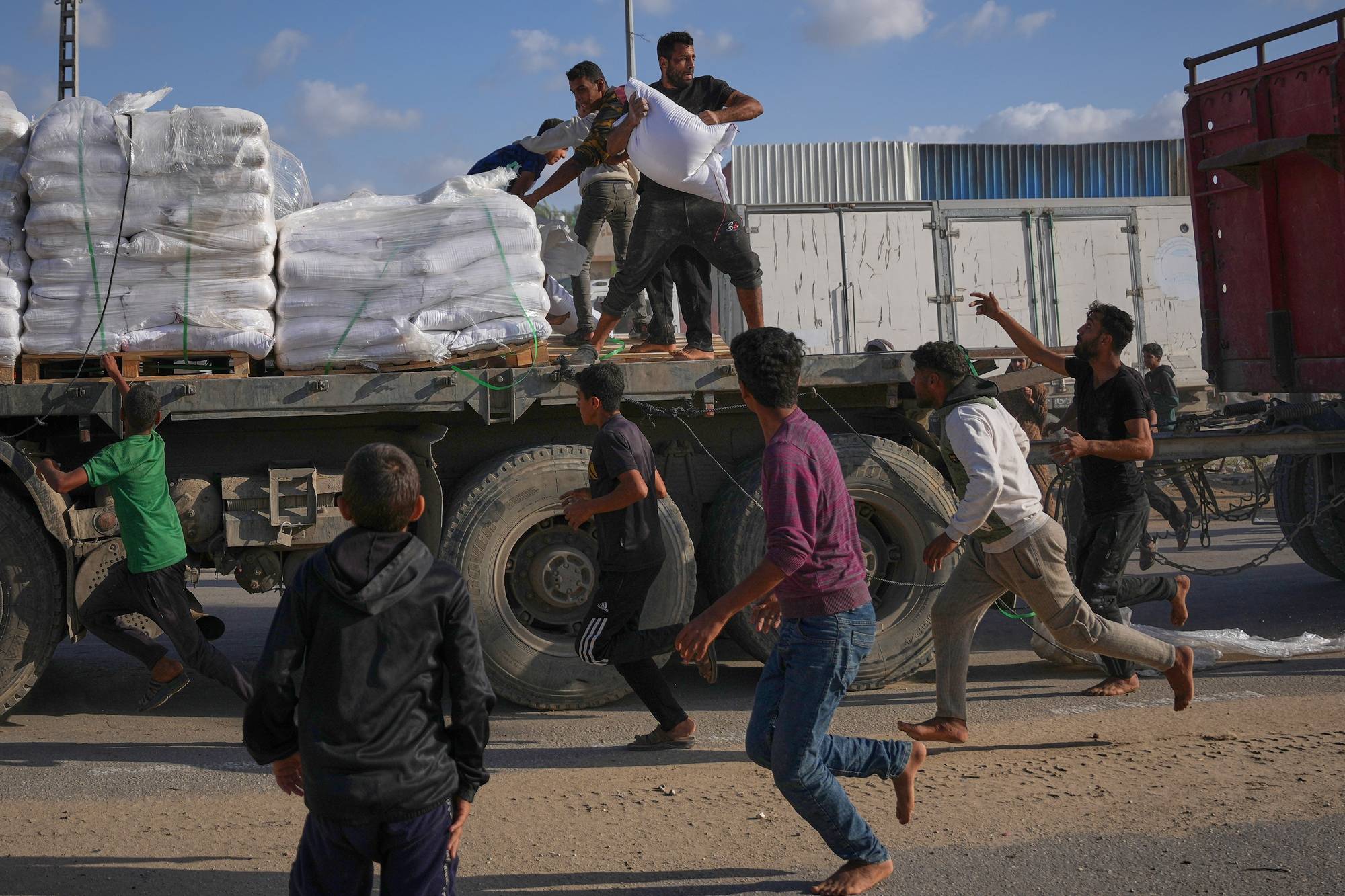 Flere palestinere løper for å hente sekker med mel fra en lastebil. De går barbeint, med bukser og tynne gensere. 