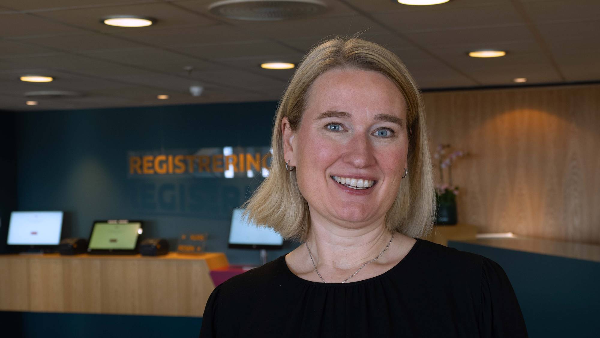 Ylva Erbach i Tekstilpro. En kvinne med blondt hår og sort genser står og smiler. 
