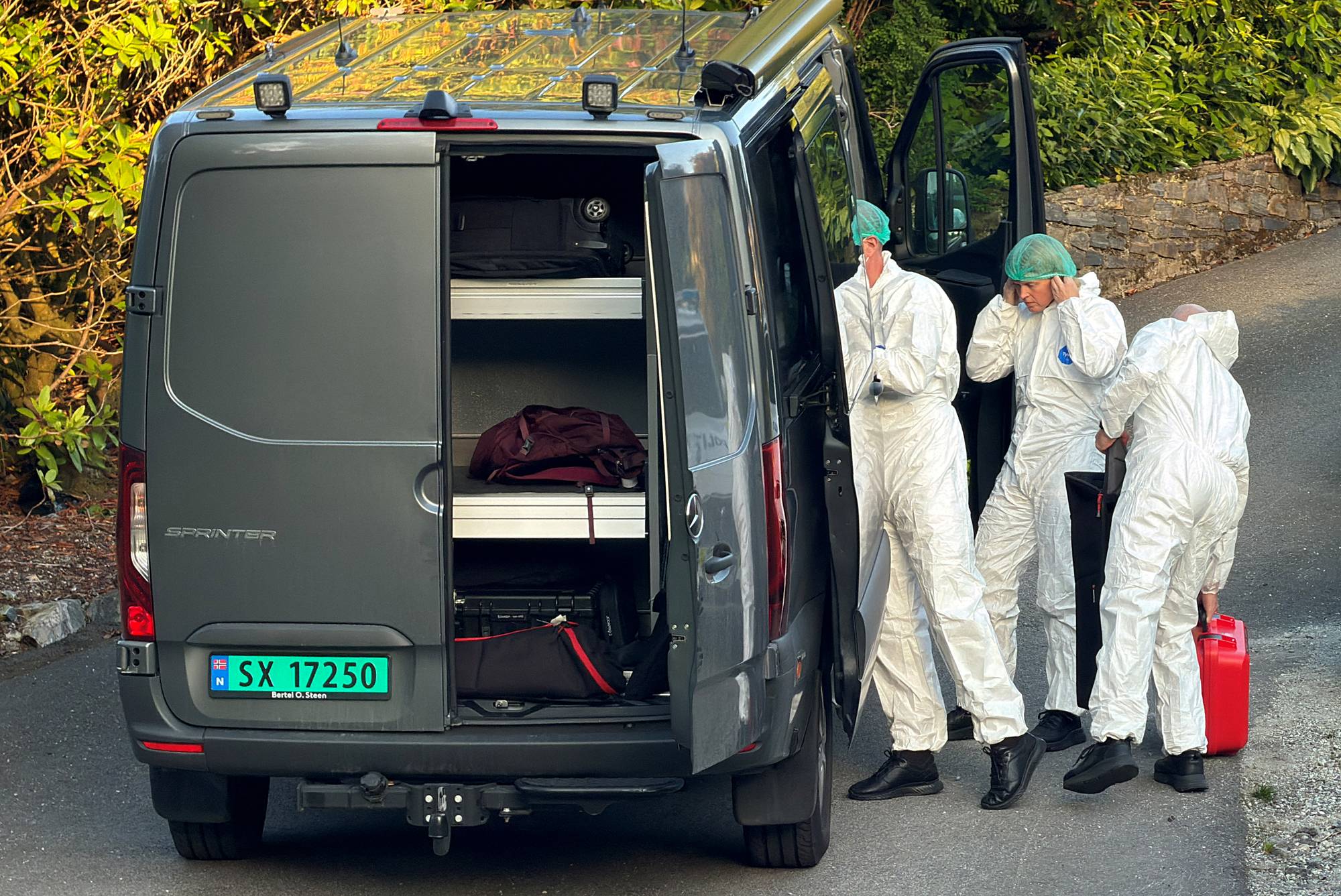 Tre personer i hvite vernedresser ved en grå varebil med åpen dør og utstyr. 