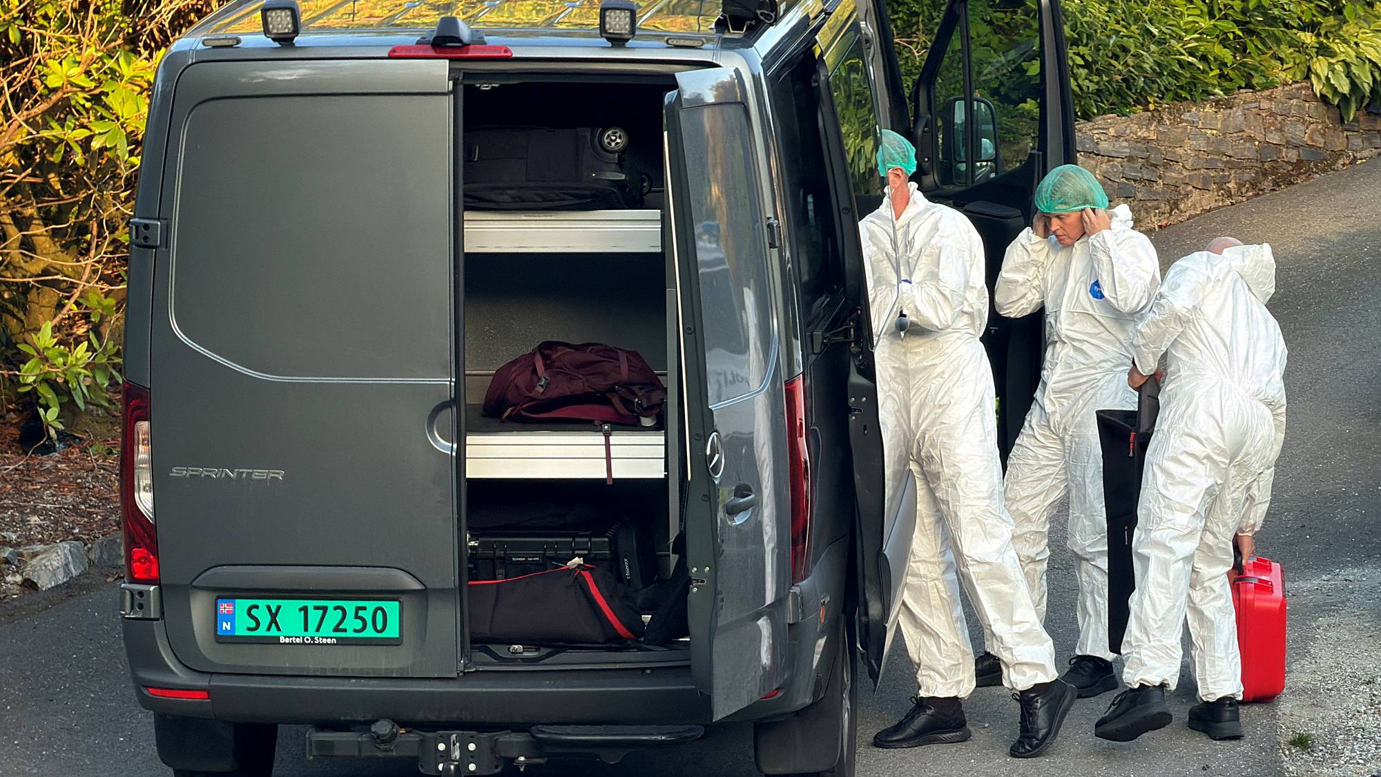 Tre personer i hvite vernedresser ved en grå varebil med åpen dør og utstyr. 