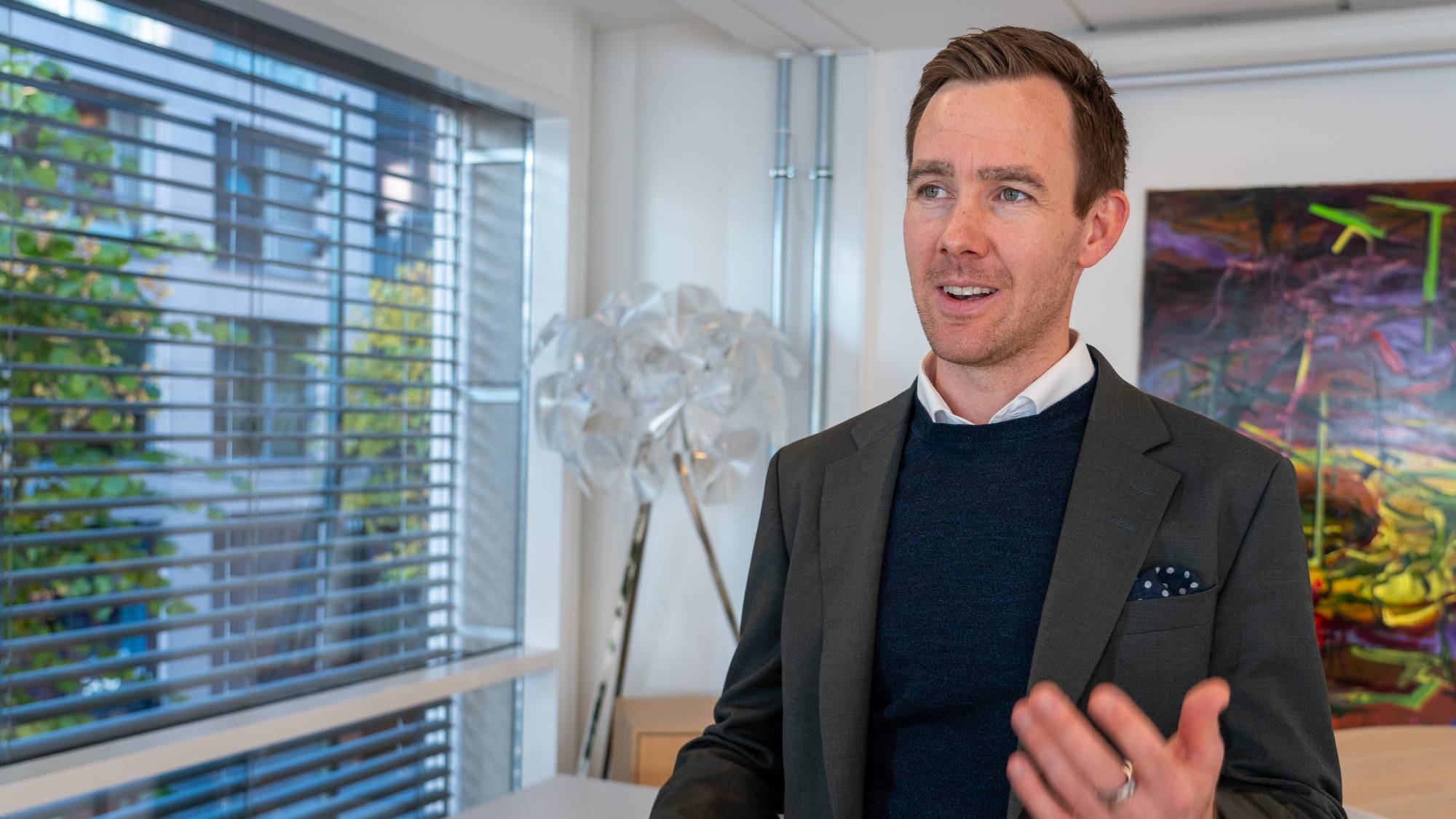 Mann med blazer forklarer noe inne på et kontor.
