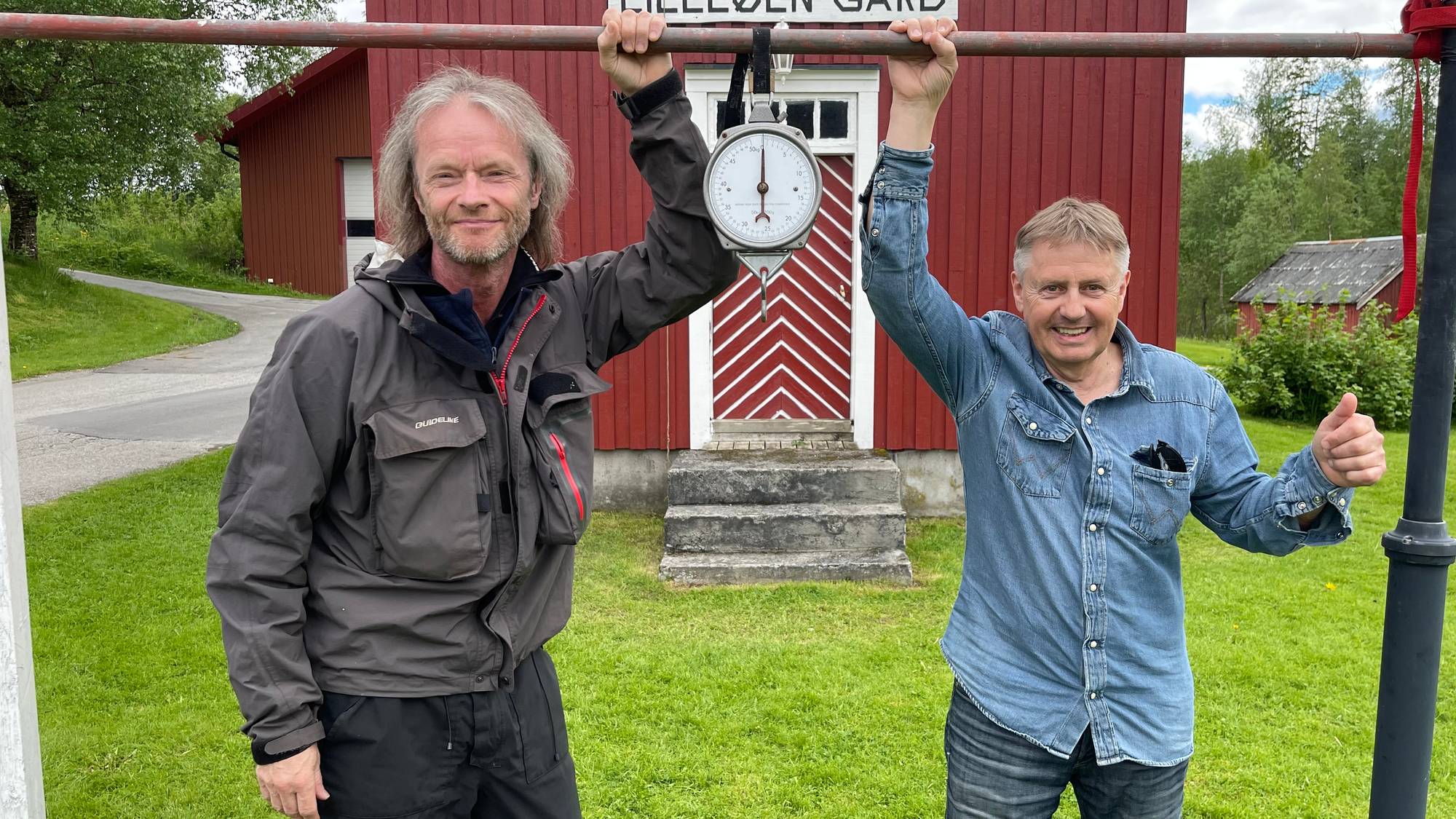 Rocker Torstein Flakne står sammen med grunneier ved Namsen i Overhalla, Svein Romundstad. De holder på en laksevekt og ser veldig fornøyde ut. 