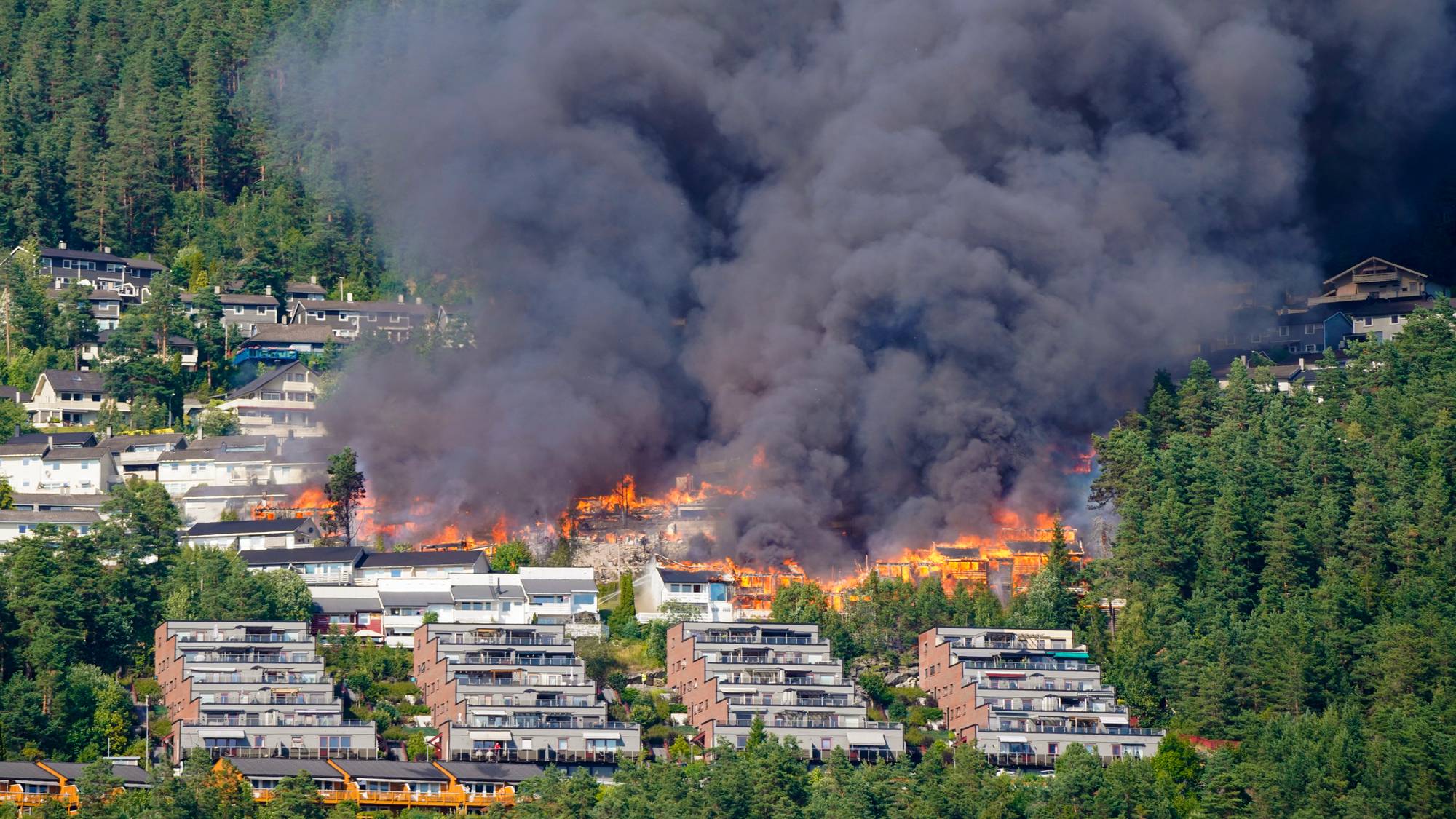 Kraftig brann med store flammer og tykk røyk i et boligområde i en skråning. (Bildebeskrivelsen er laget av en KI-tjeneste)