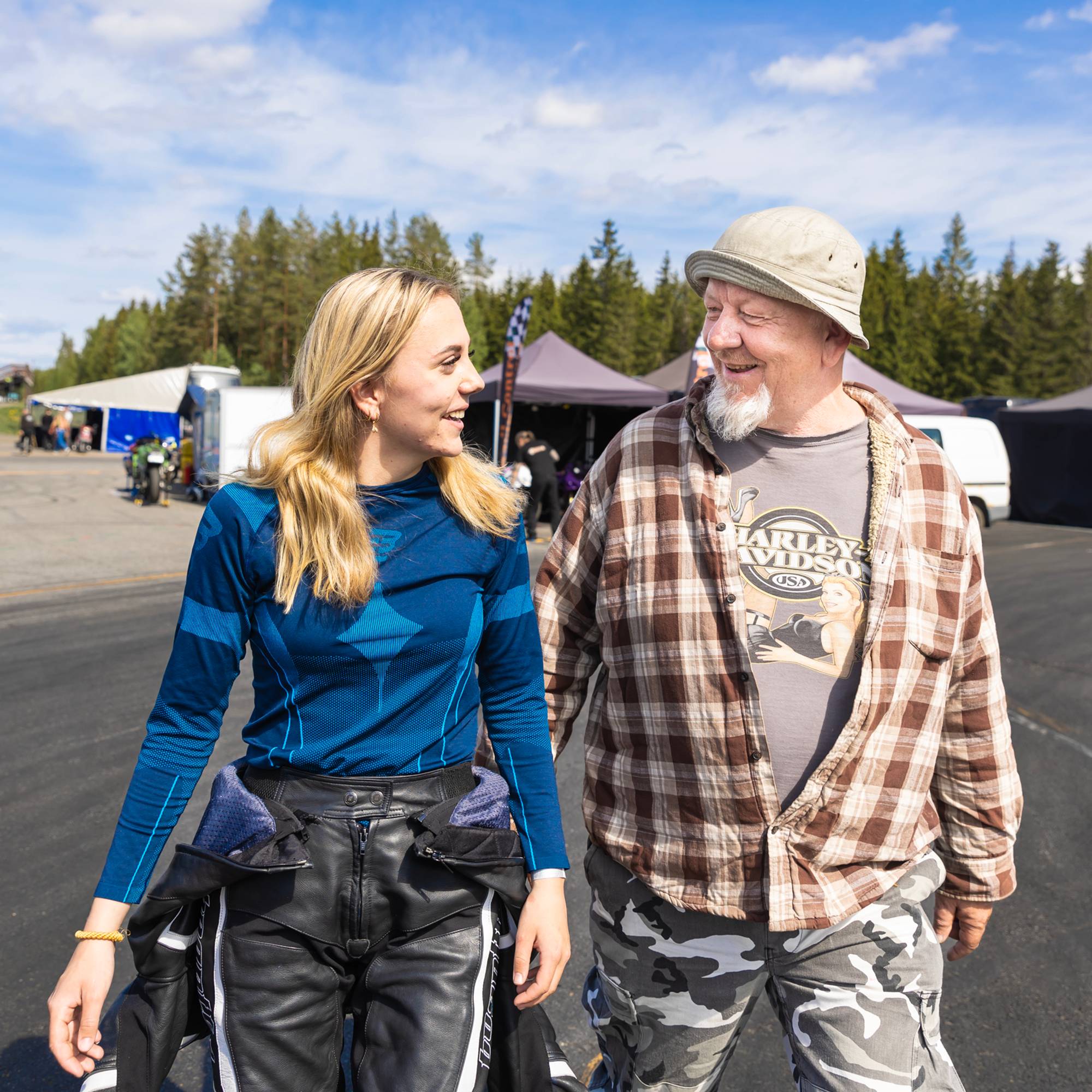 Sarah og pappaen hennes smiler mot hverandre mens de går bortover den varme asfalten på Gardermoen Raceway.