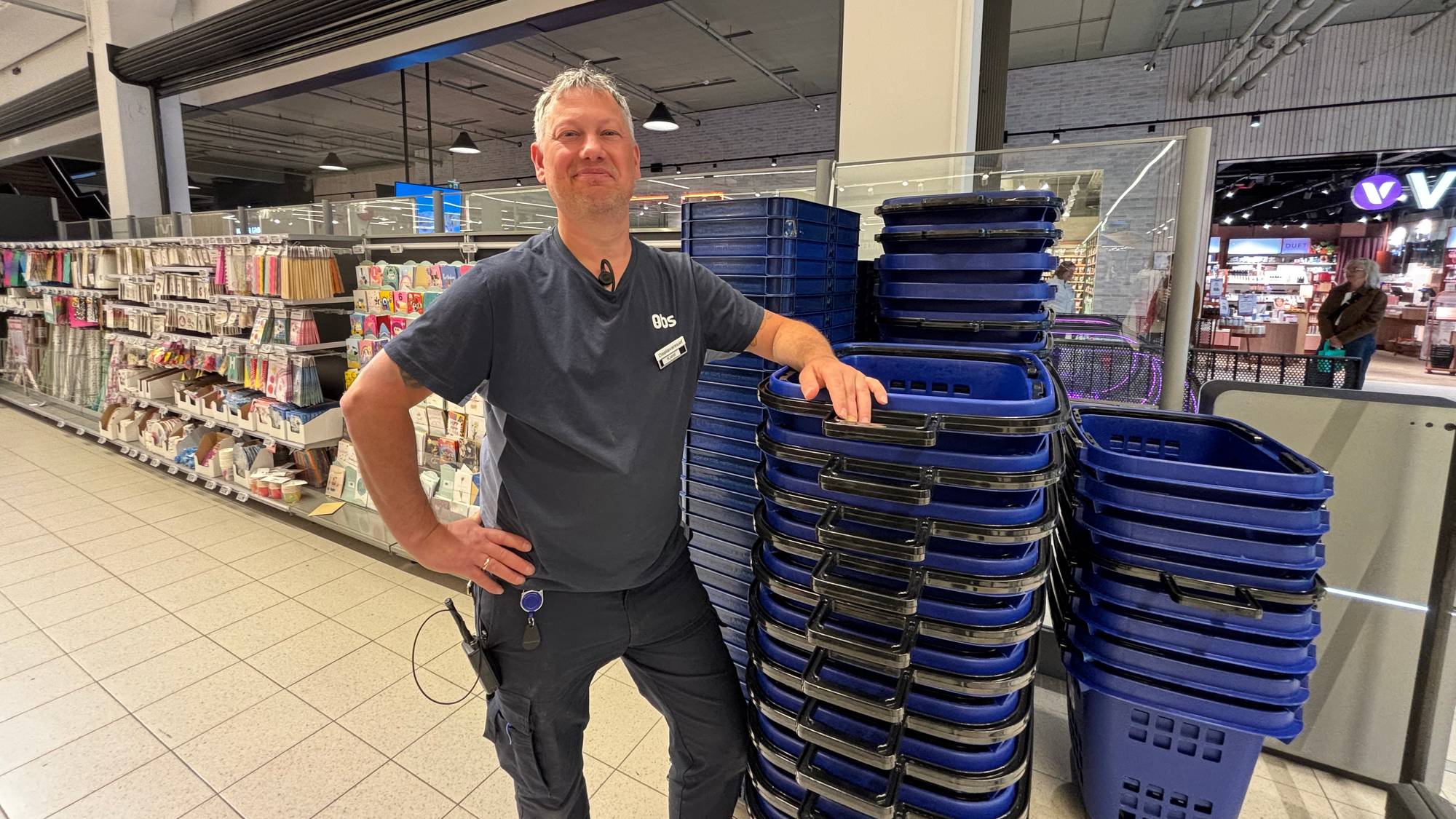 En person i mørke klær står ved siden av flere blå handlekurver