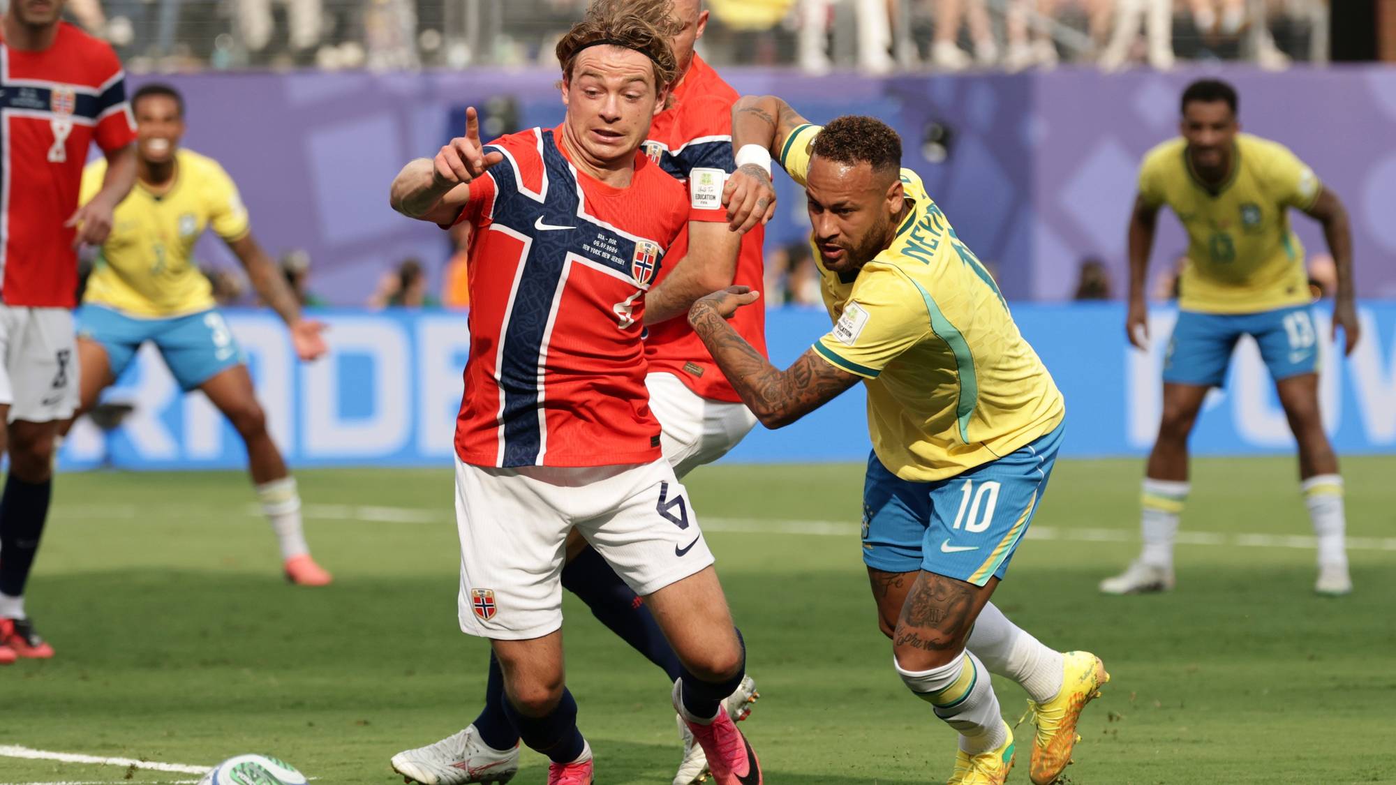 Norsk og brasiliansk fotballspiller kjemper om ballen på gressbanen under en landskamp. (Bildebeskrivelsen er laget av en KI-tjeneste)