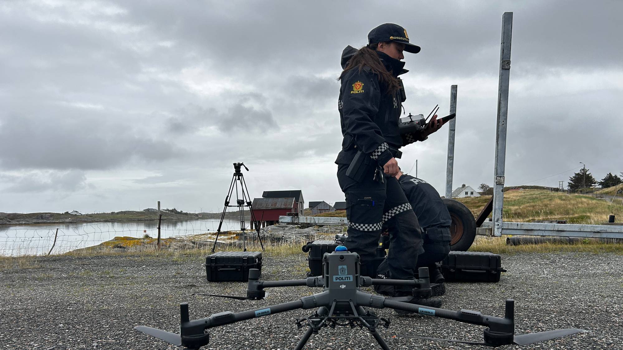 Politibetjenter bruker en drone ved et havneområde i gråvær. (Bildebeskrivelsen er laget av en KI-tjeneste)