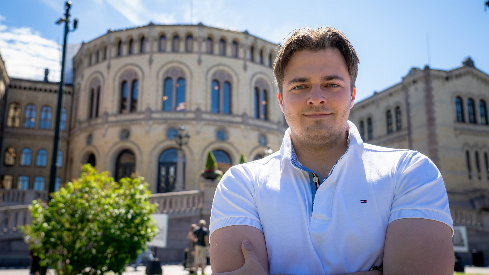 En mann med hvit pikéskjorte står foran Stortingsbygningen i Oslo. (Bildebeskrivelsen er laget av en KI-tjeneste)