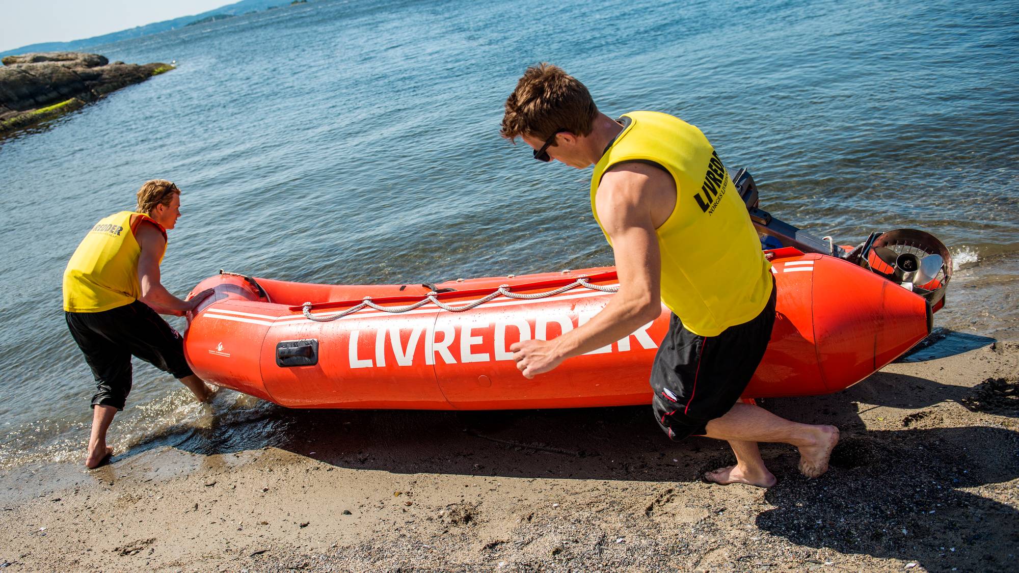 en gruppe mennesker som bærer et surfebrett på en strand