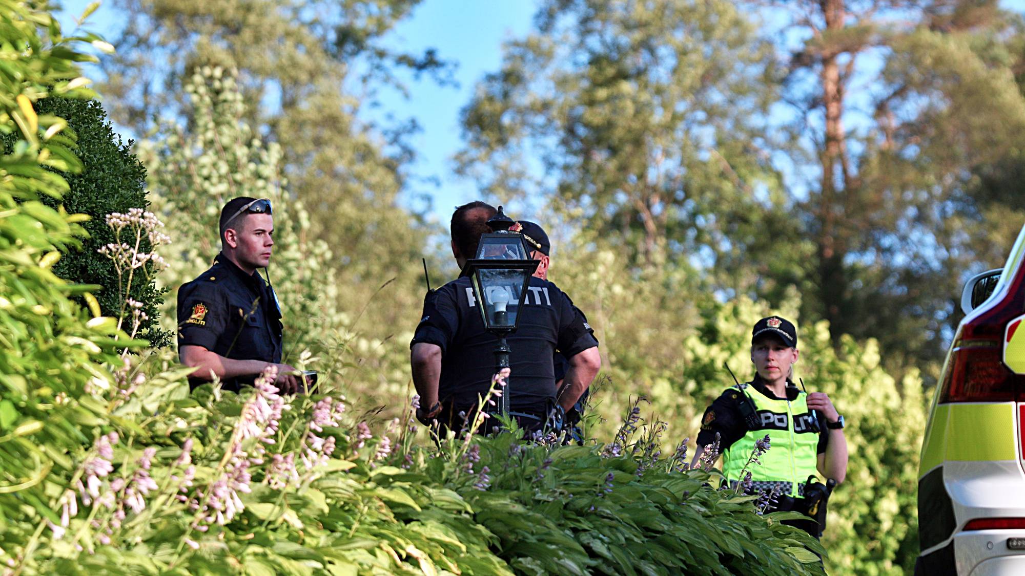 Norsk politi patruljerer i et grønt uteområde ved en politibil. 