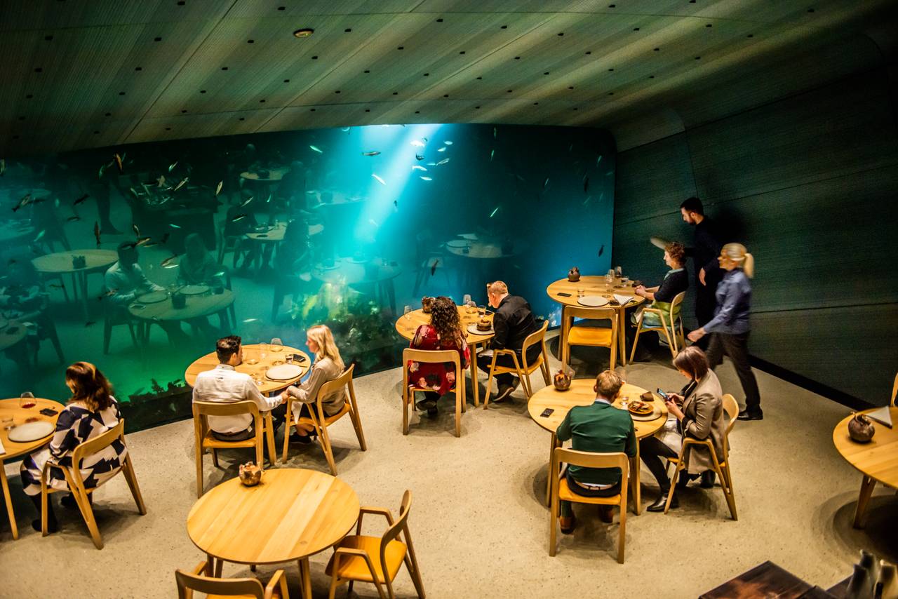Folk sitter og spiser på Undervannsrestauranten Under mens fisk svømmer utenfor vinduet