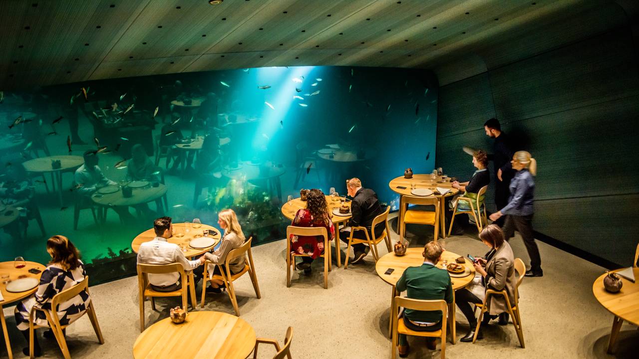 Folk sitter og spiser på Undervannsrestauranten Under mens fisk svømmer utenfor vinduet