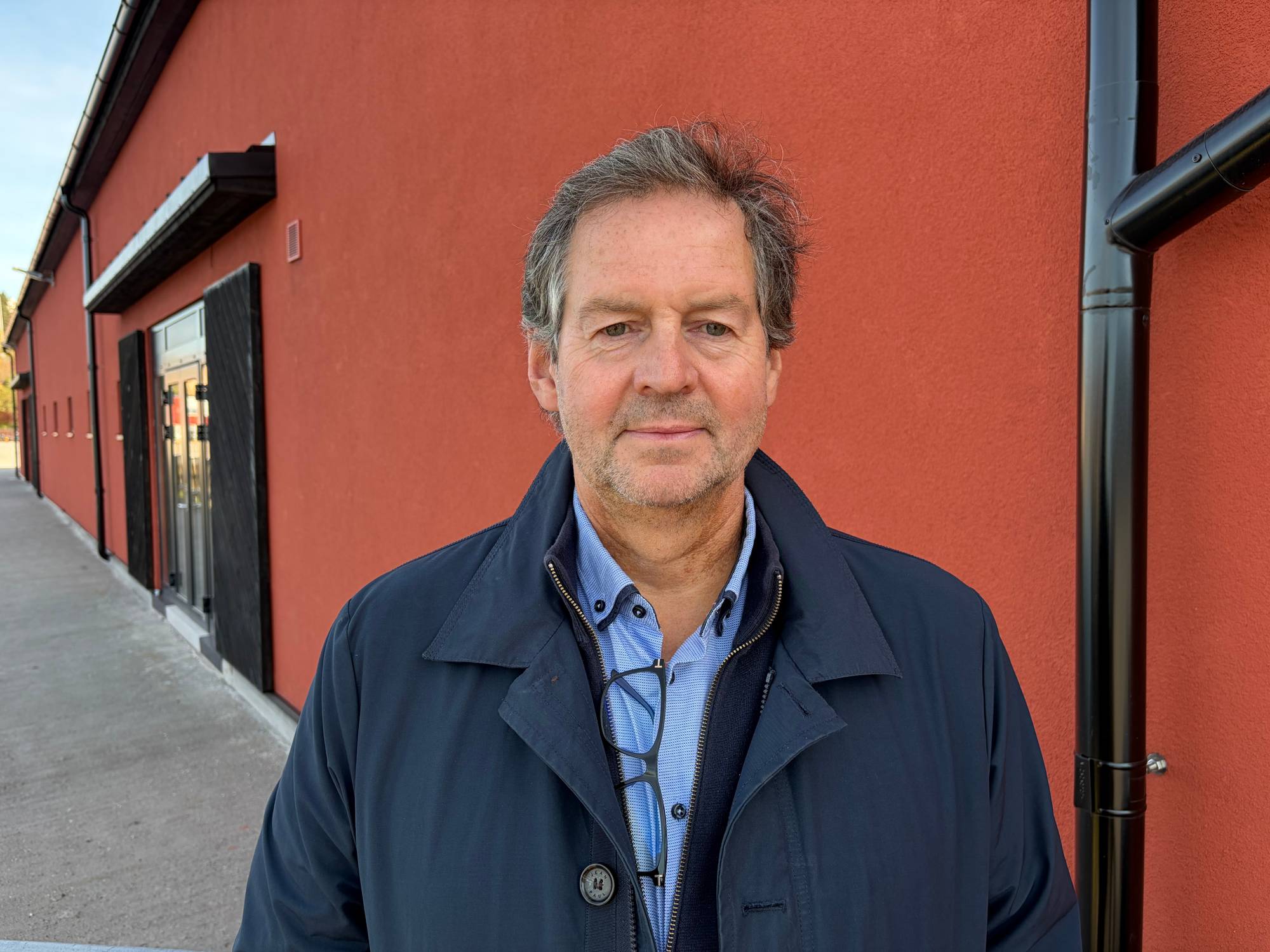 Portrett av en middelaldrende mann foran en rød bygningsvegg. (Bildebeskrivelsen er laget av en KI-tjeneste)