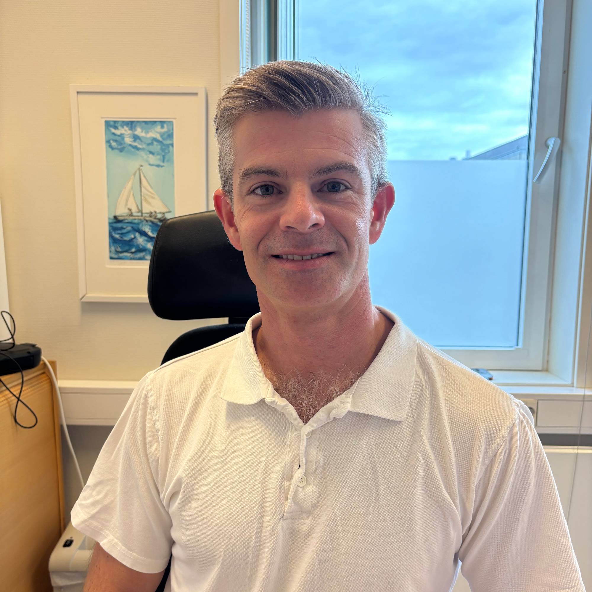 En mann med hvit skjorte ser rett inn i kameraet. Han sitter på et kontor.