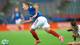 Thomas Andersen / NTB En fotballspiller i blå drakt løper med ballen på en grønn gressmatte. En annen spiller i hvit drakt ligger på bakken. Kampen spilles på en stadion med tribuner i bakgrunnen. (Bildebeskrivelsen er laget av en KI-tjeneste)