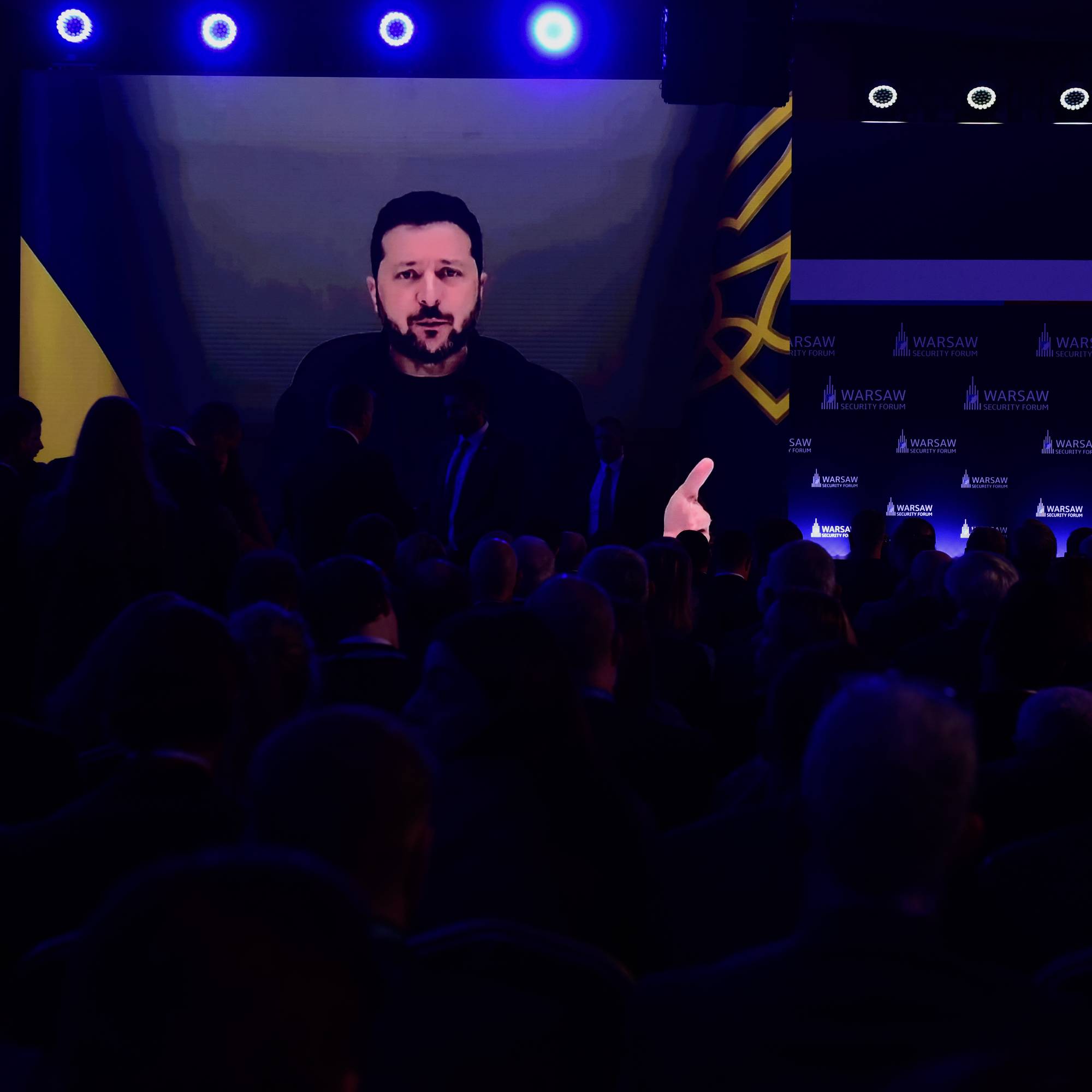 Volodymyr Zelenskyj taler via storskjerm til en forsamling under Warsaw Security Forum. (Bildebeskrivelsen er laget av en KI-tjeneste)