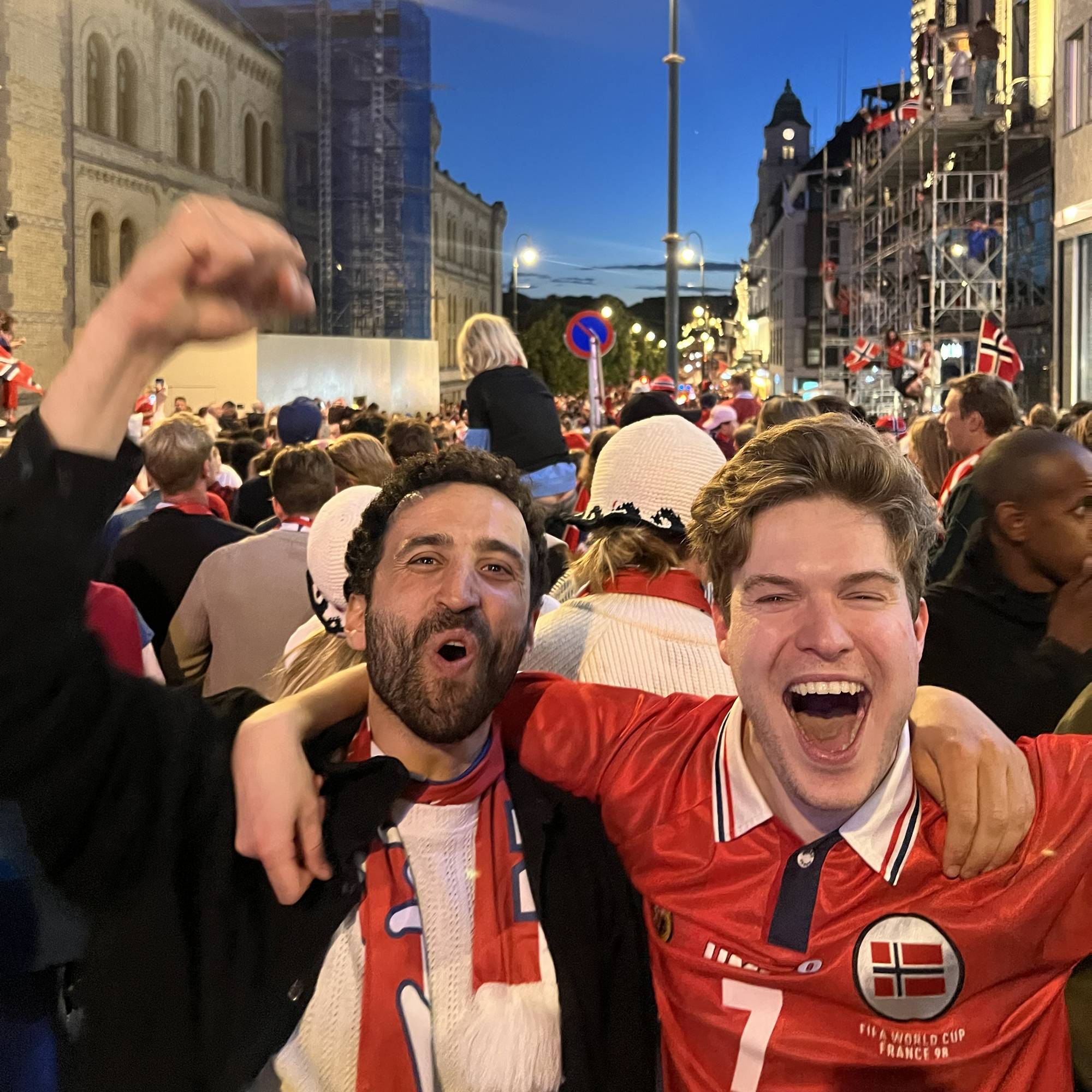 To menn står i en folkemengde på Karl Johan og jubler. Den ene mannen har på norsk fotballskjerf og den andre mannen har på en norsk landslagsdrakt.
