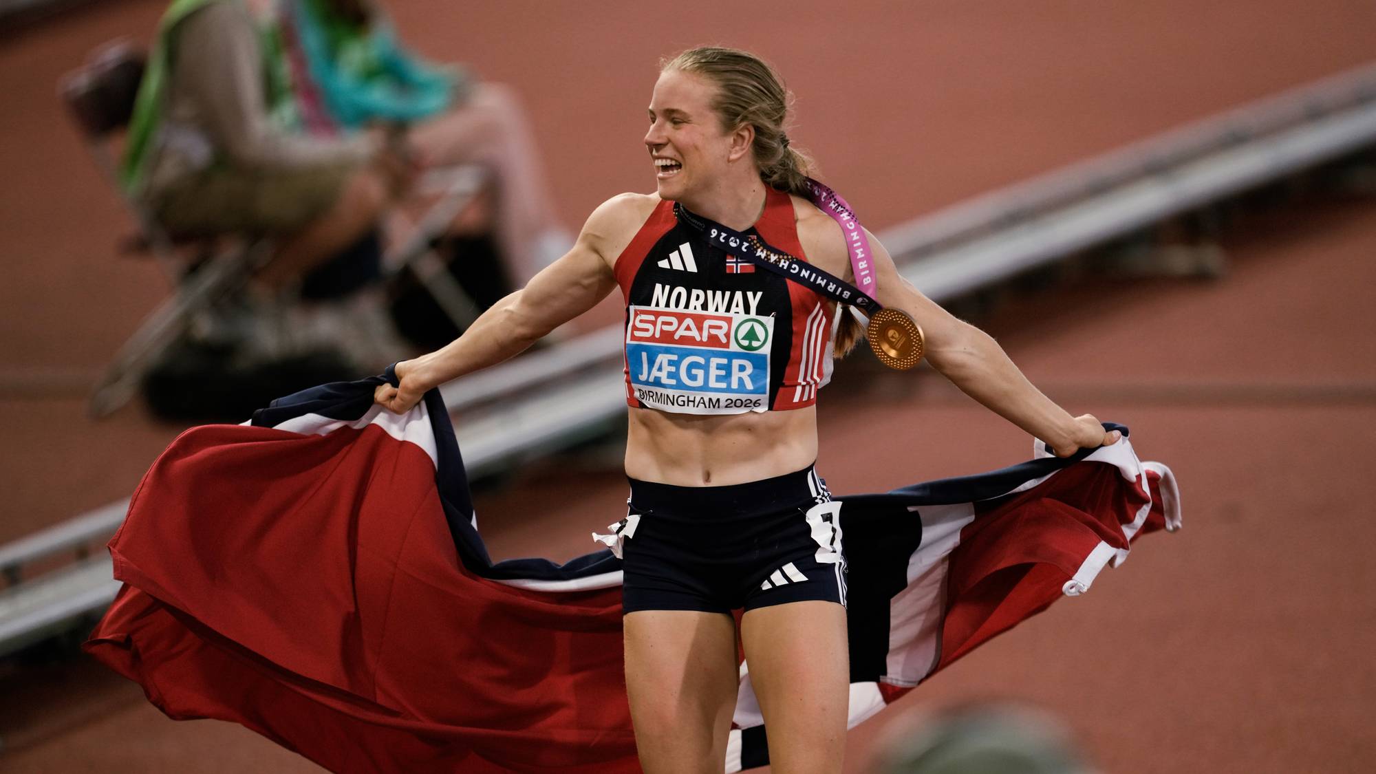 En jente med gullmedalje rundt halsen og norskt flagg rundt kroppen.