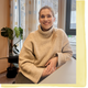 Kvinne sitter ved pulten. Hun ser i kamera og smiler.