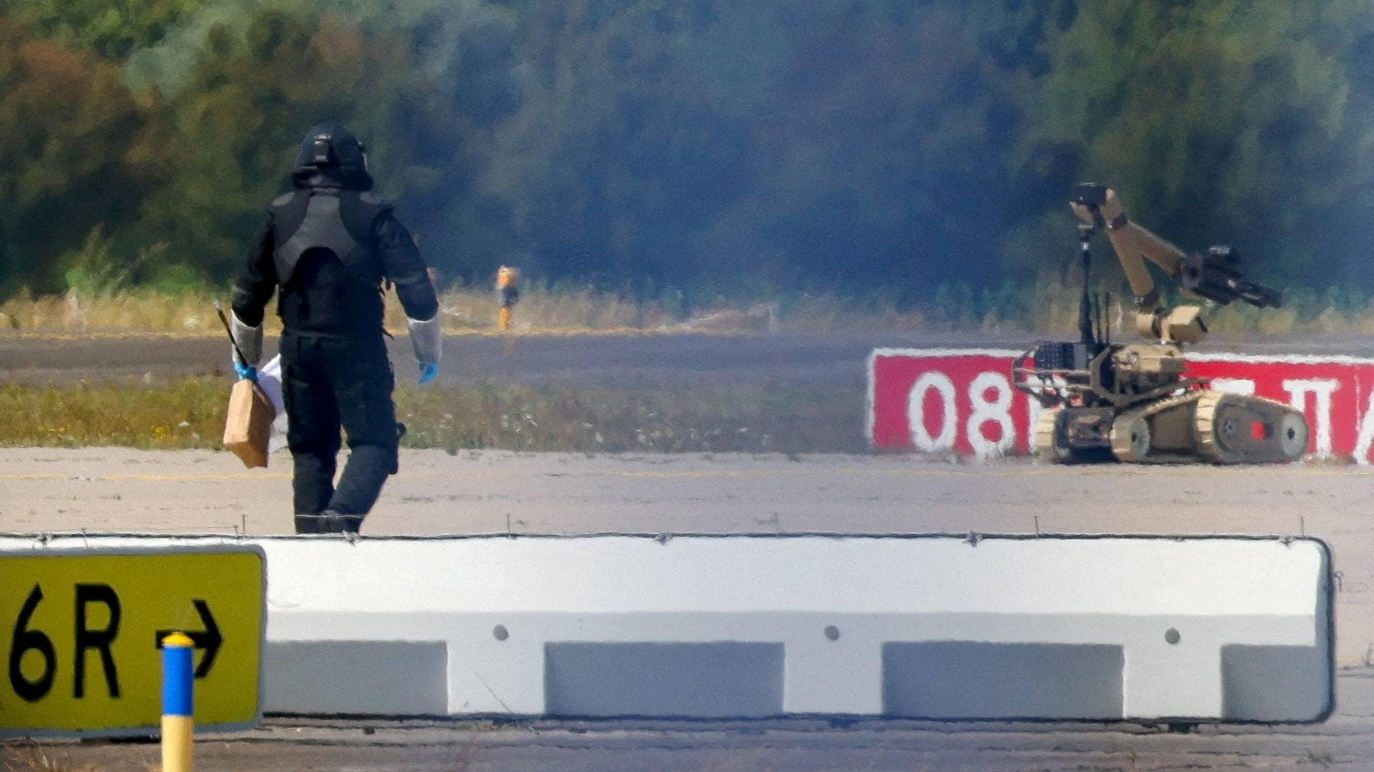 A police officer in protective clothing walks next to an explosive-disarming robot (EOD) at Leipzig/Halle Airport