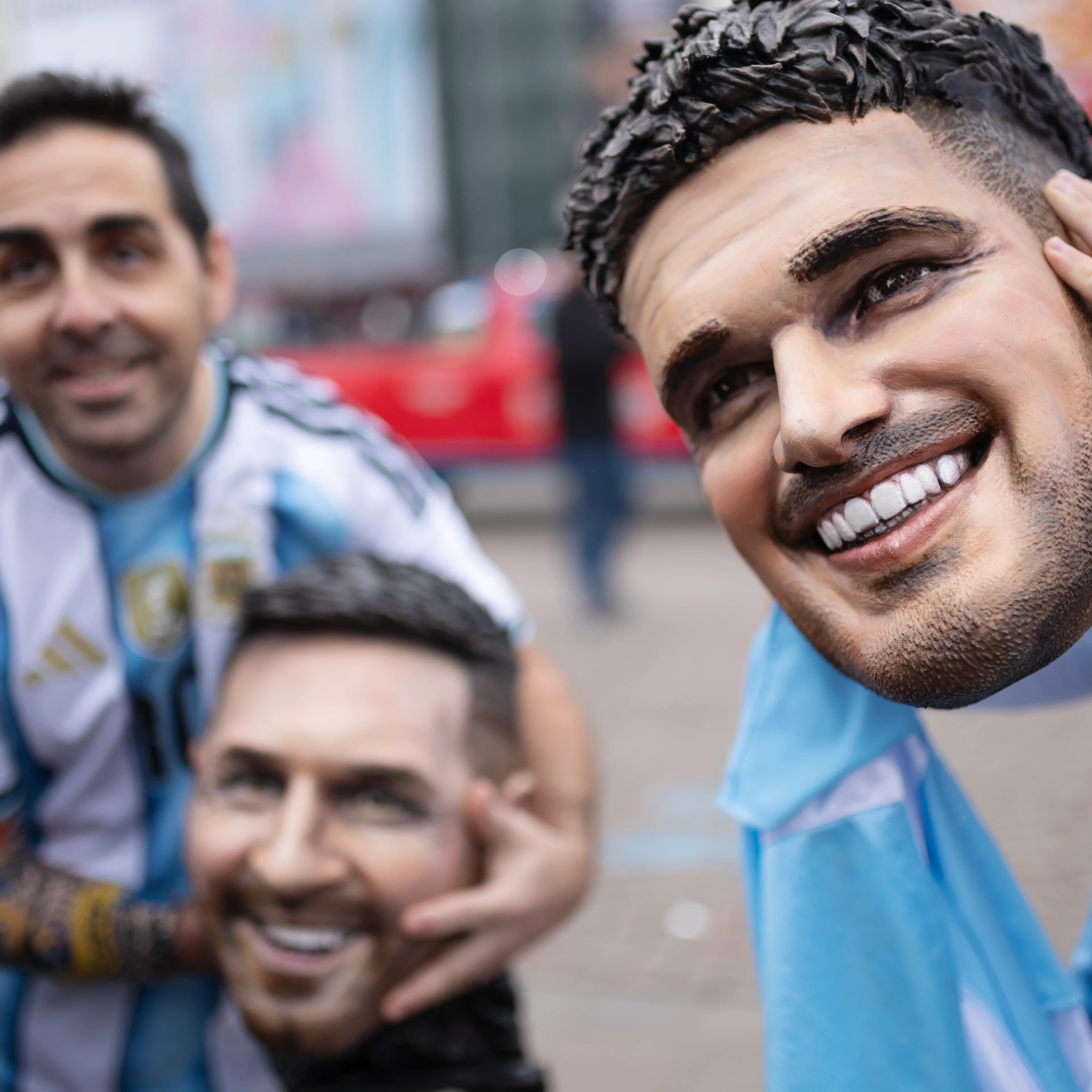 Personer i argentinske landslagsdrakter holder opp store masker av fotballspillere.