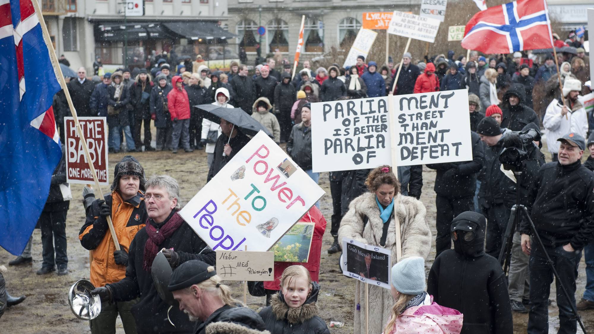 Demonstranter med flagg og plakater samlet på en plass i Reykjavik i snøvær. (Bildebeskrivelsen er laget av en KI-tjeneste)