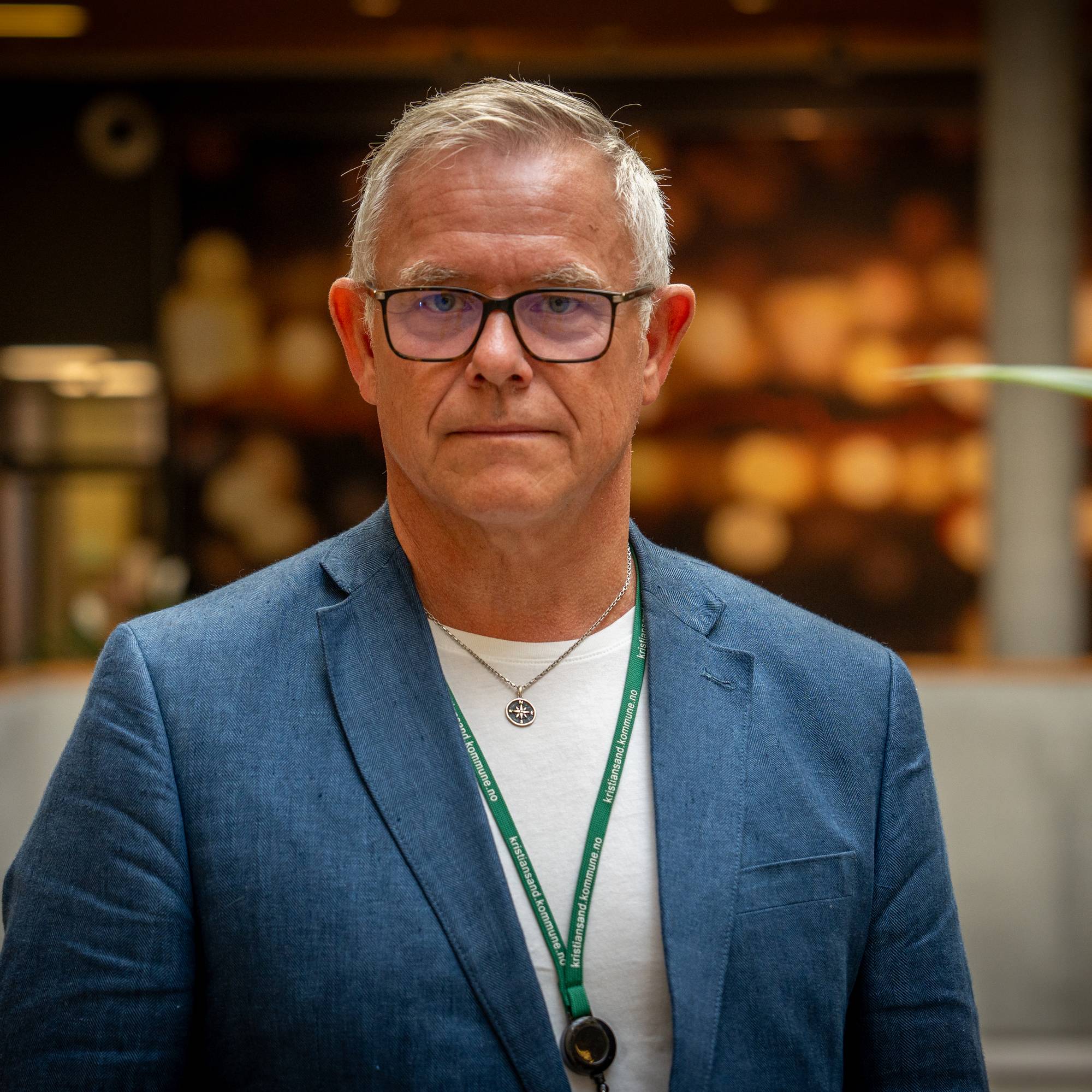 Portrett av en mann med briller og blå blazer, stående innendørs foran en uskarp bakgrunn. (Bildebeskrivelsen er laget av en KI-tjeneste)