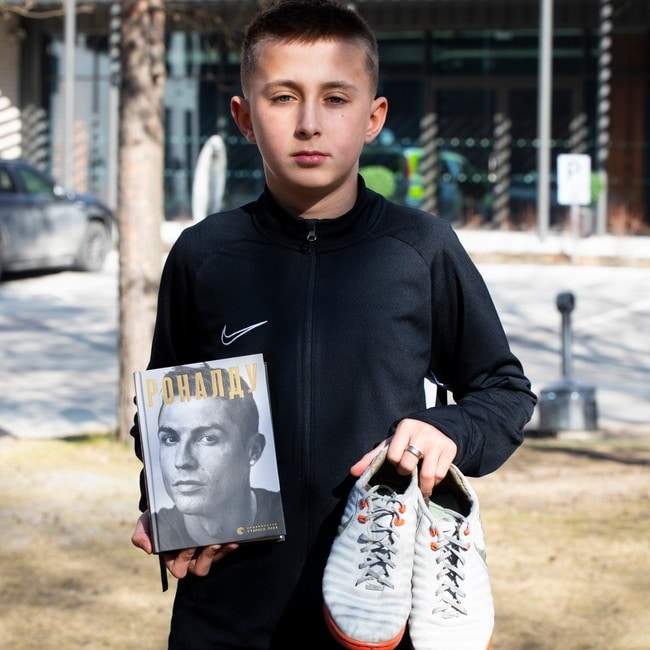 Ukrainsk gutt viser frem boka og fotballskoene han fikk med seg til Norge. 