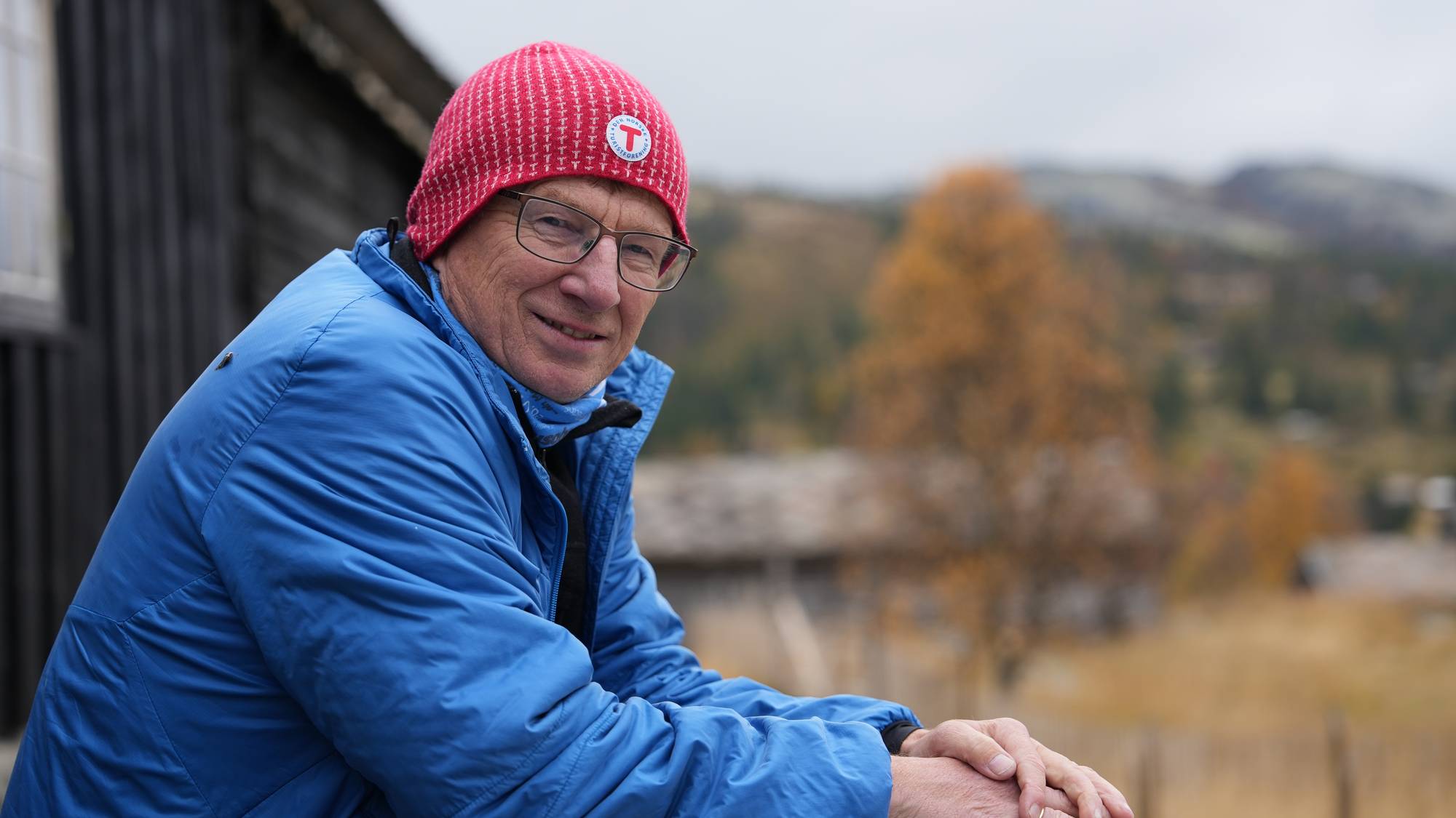 en mann iført en blå jakke, rød lue og briller sitter ved et bord