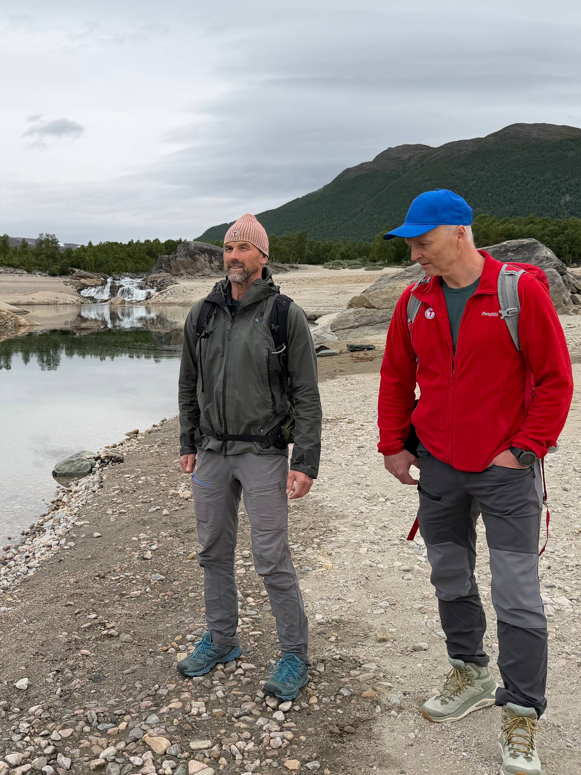 To menn står med hendene i lomma ved strandkanten til Gjevilvatnet i Oppdal kommune i Trøndelag. 