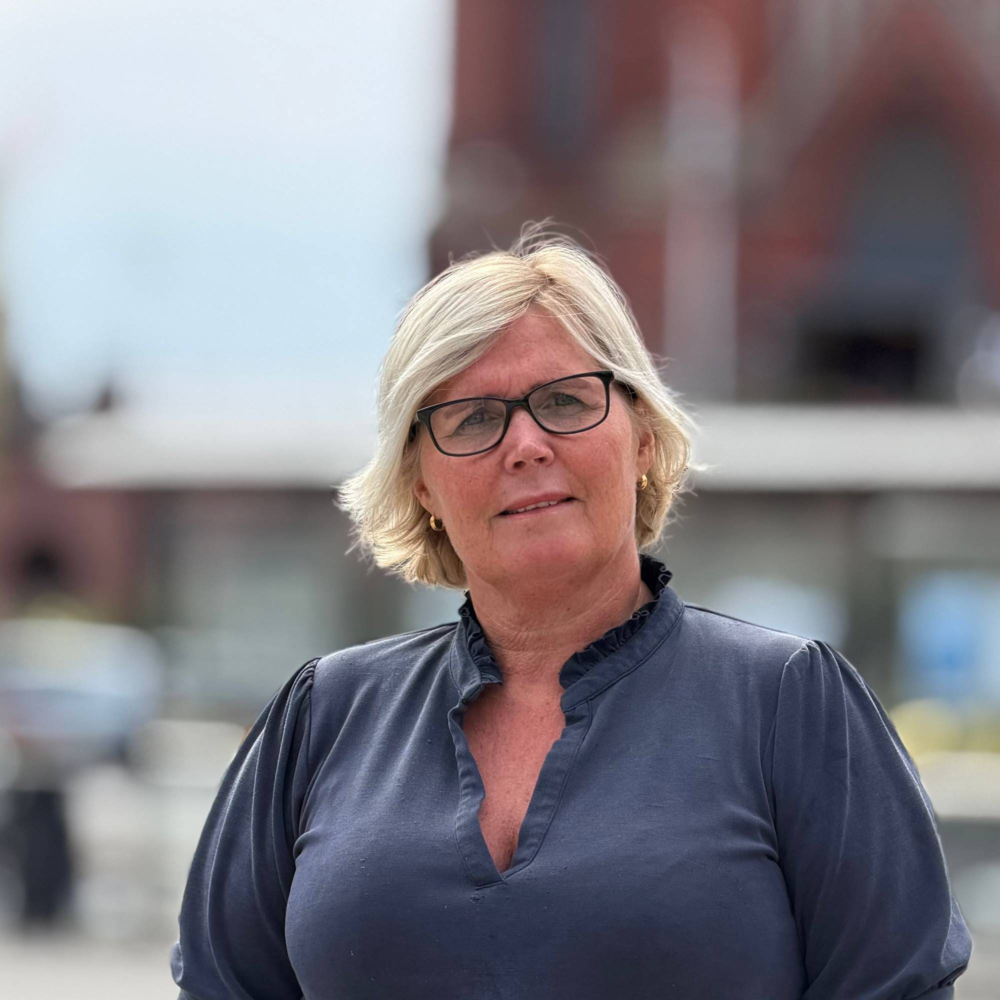 Kvinne med lyst hår og blå genser med kirke i bakgrunnen
