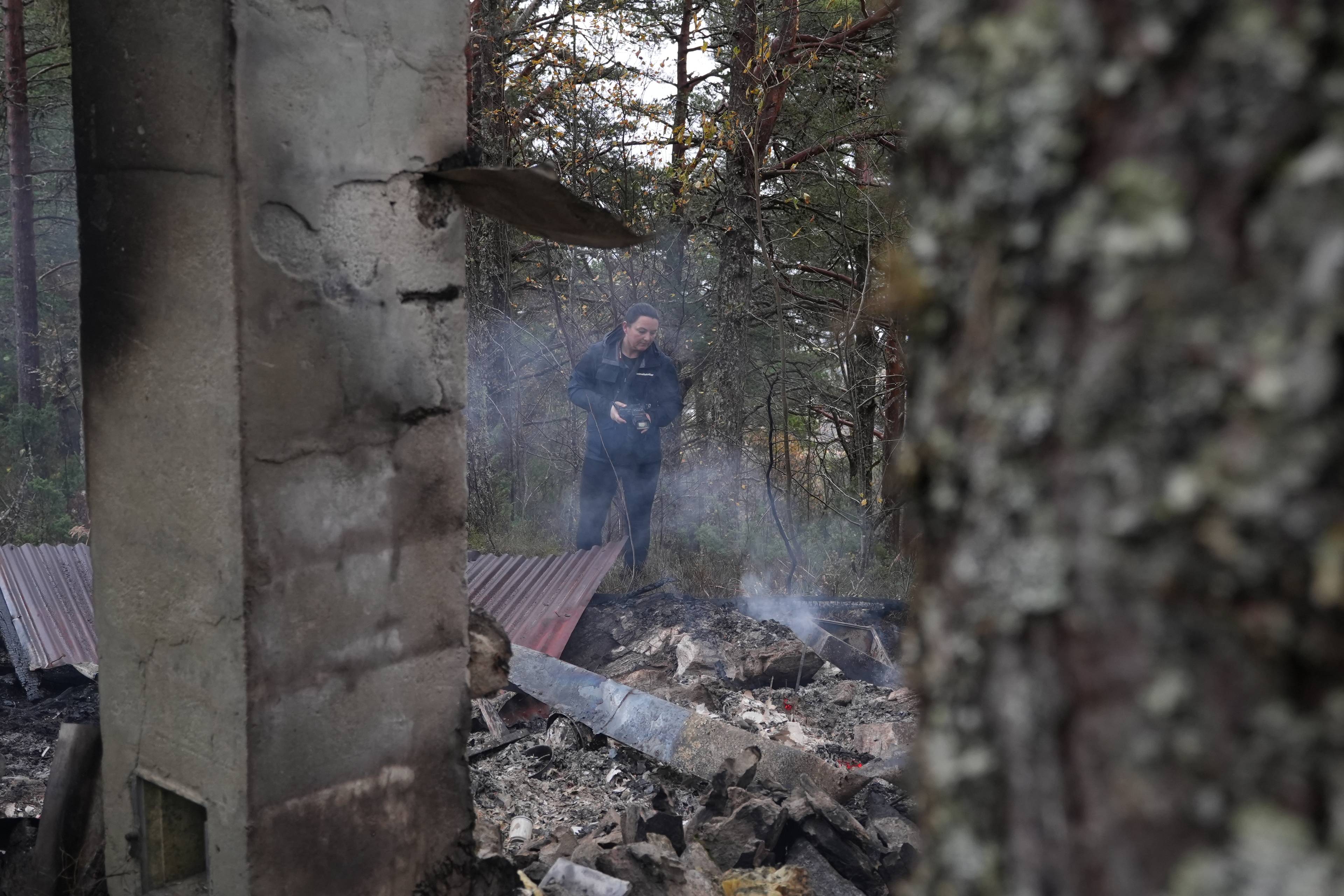 Person undersøker branntomt etter brent bygning i skogsområde.