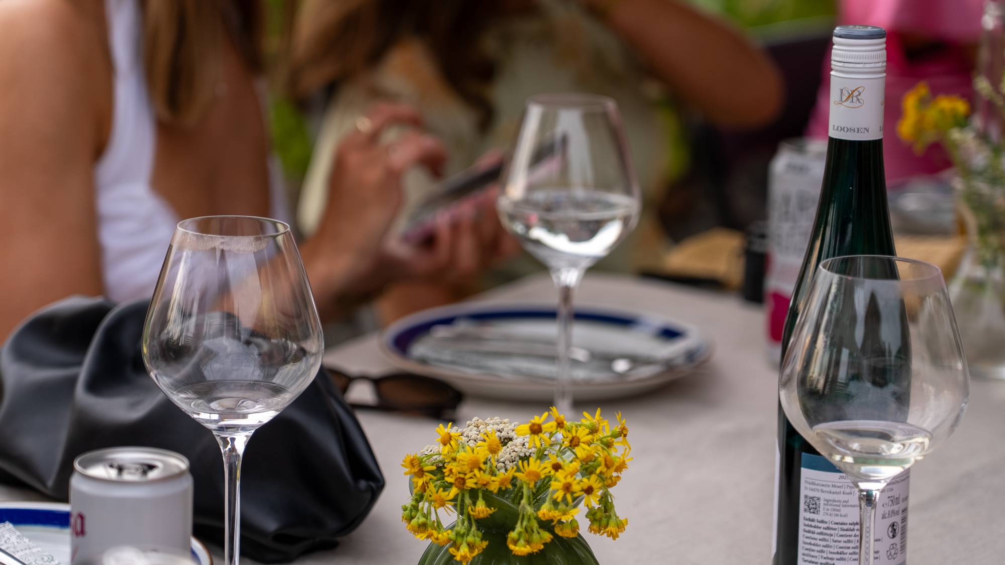 Vinglass og en vinflaske på et bord dekket med blomster og serveringsartikler. (Bildebeskrivelsen er laget av en KI-tjeneste)