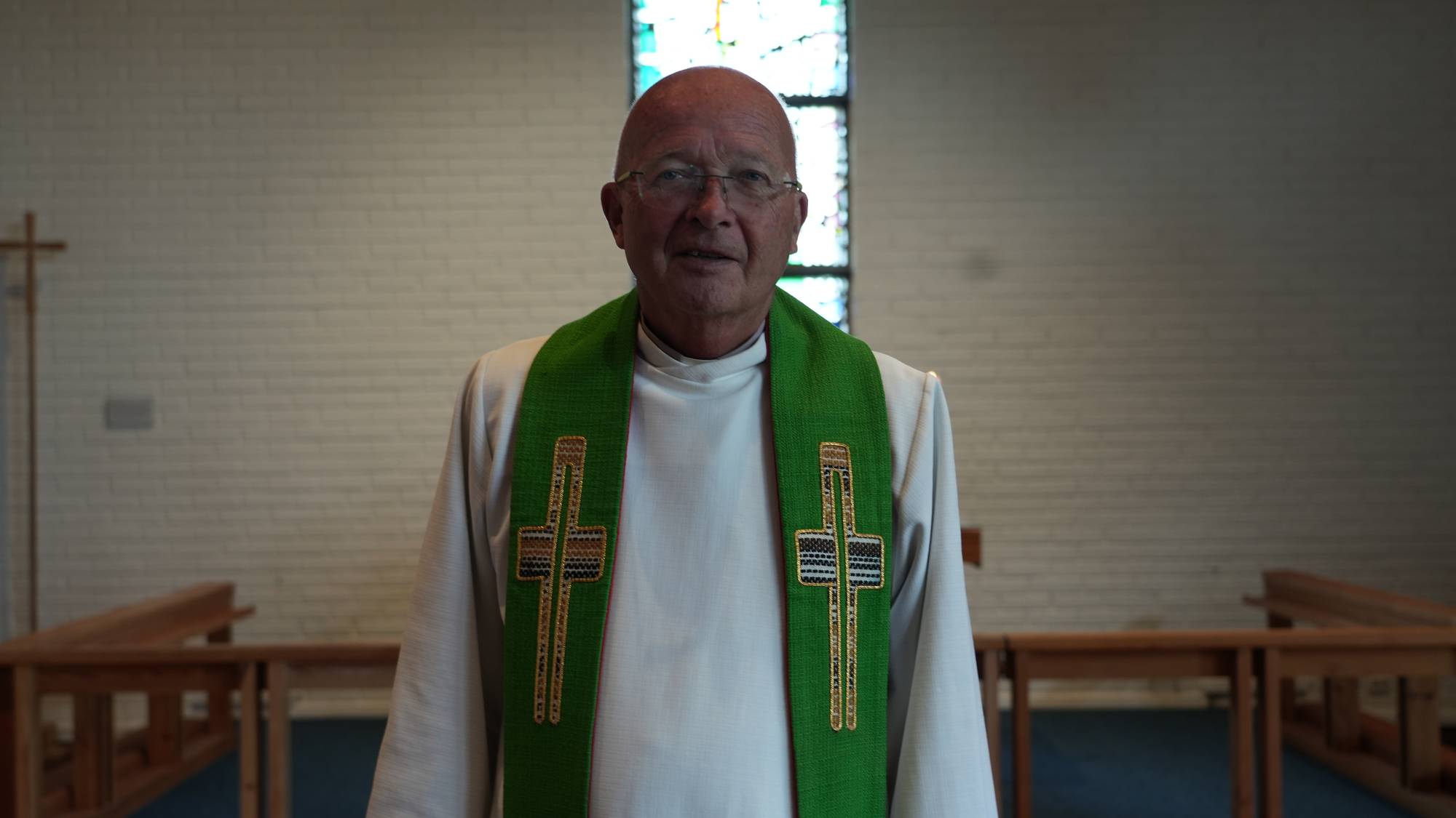 En mannlig prest i hvit kappe med grønt stola står i en kirke. (Bildebeskrivelsen er laget av en KI-tjeneste)