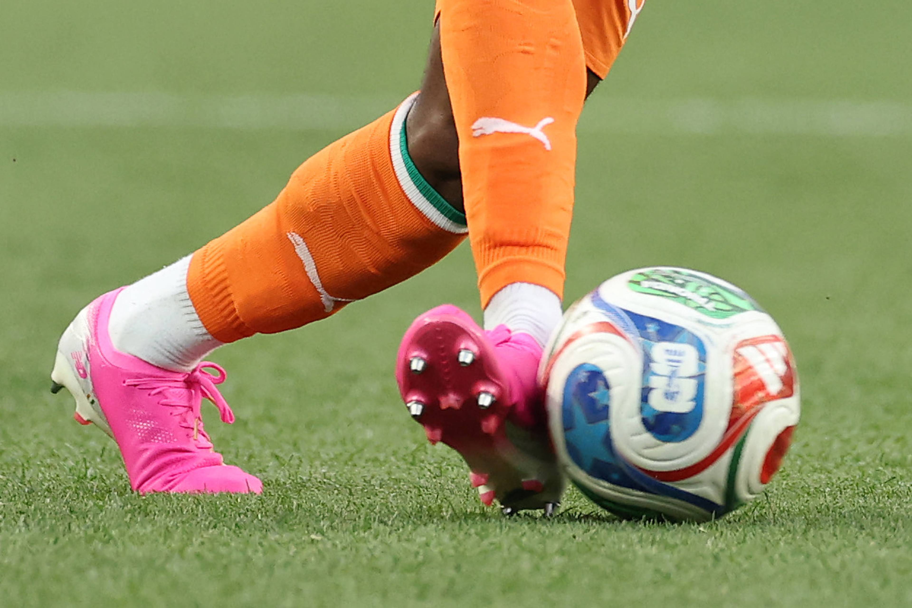 En fotballspiller i oransje drakt med nummer 11 dribler ballen på en gressbane. Spilleren har fletter og et hvitt merke på trøyen. Rundt spilleren er en fotballbane med uskarpe tilskuere i bakgrunnen. (Bildebeskrivelsen er laget av en KI-tjeneste)