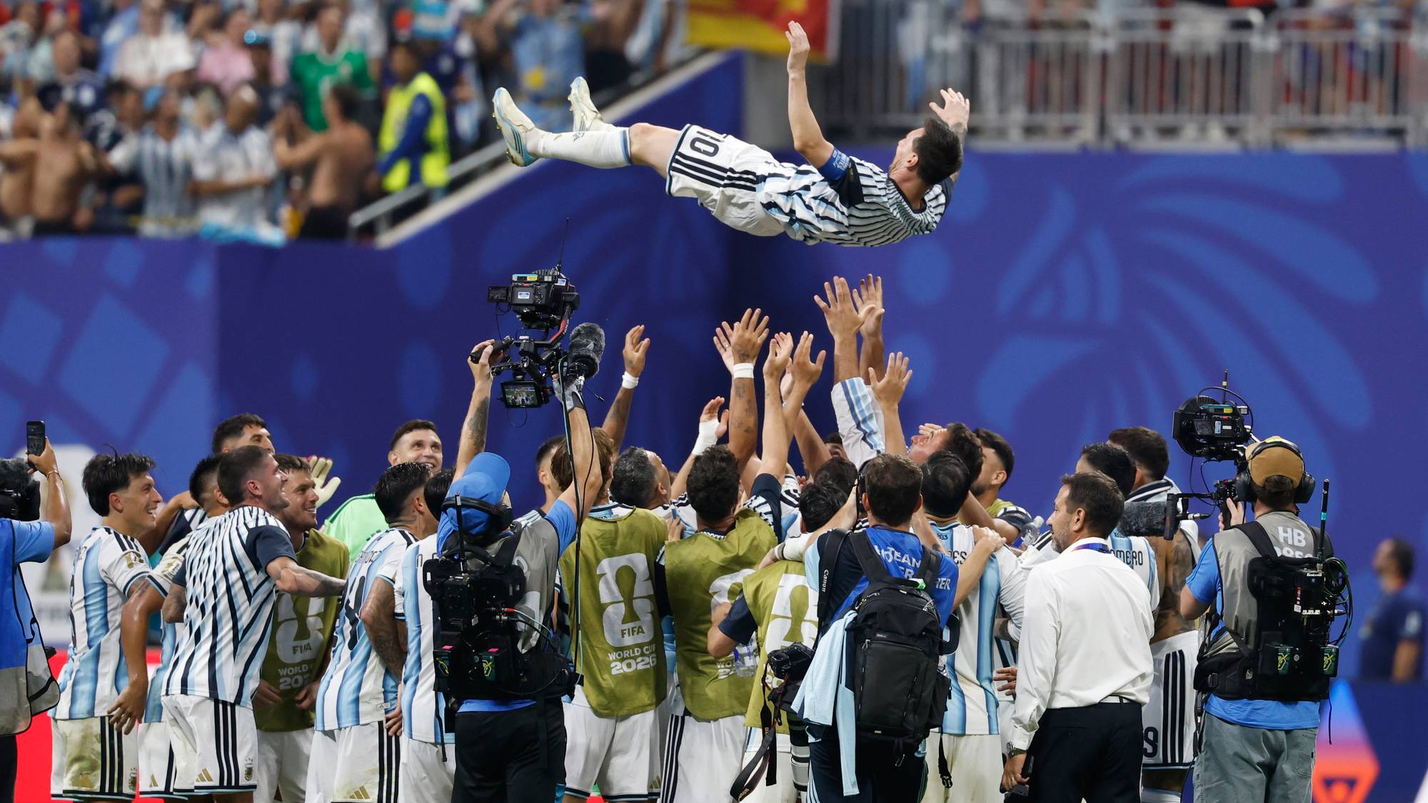 Lionel Messi kastes opp i luften av jublende lagkamerater på fotballbanen omgitt av fotografer. (Bildebeskrivelsen er laget av en KI-tjeneste)