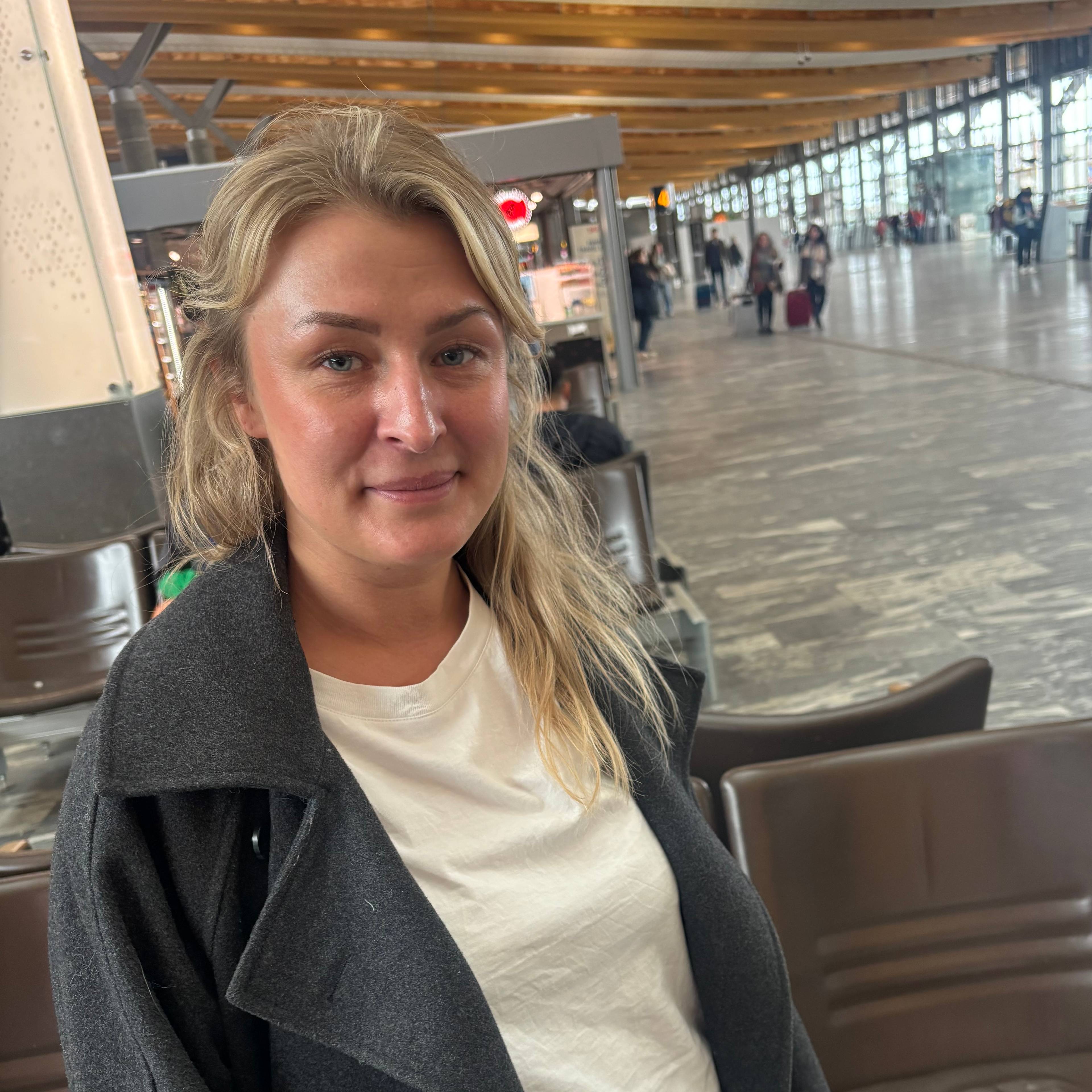 En kvinne med blondt hår sitter på en flyplass.