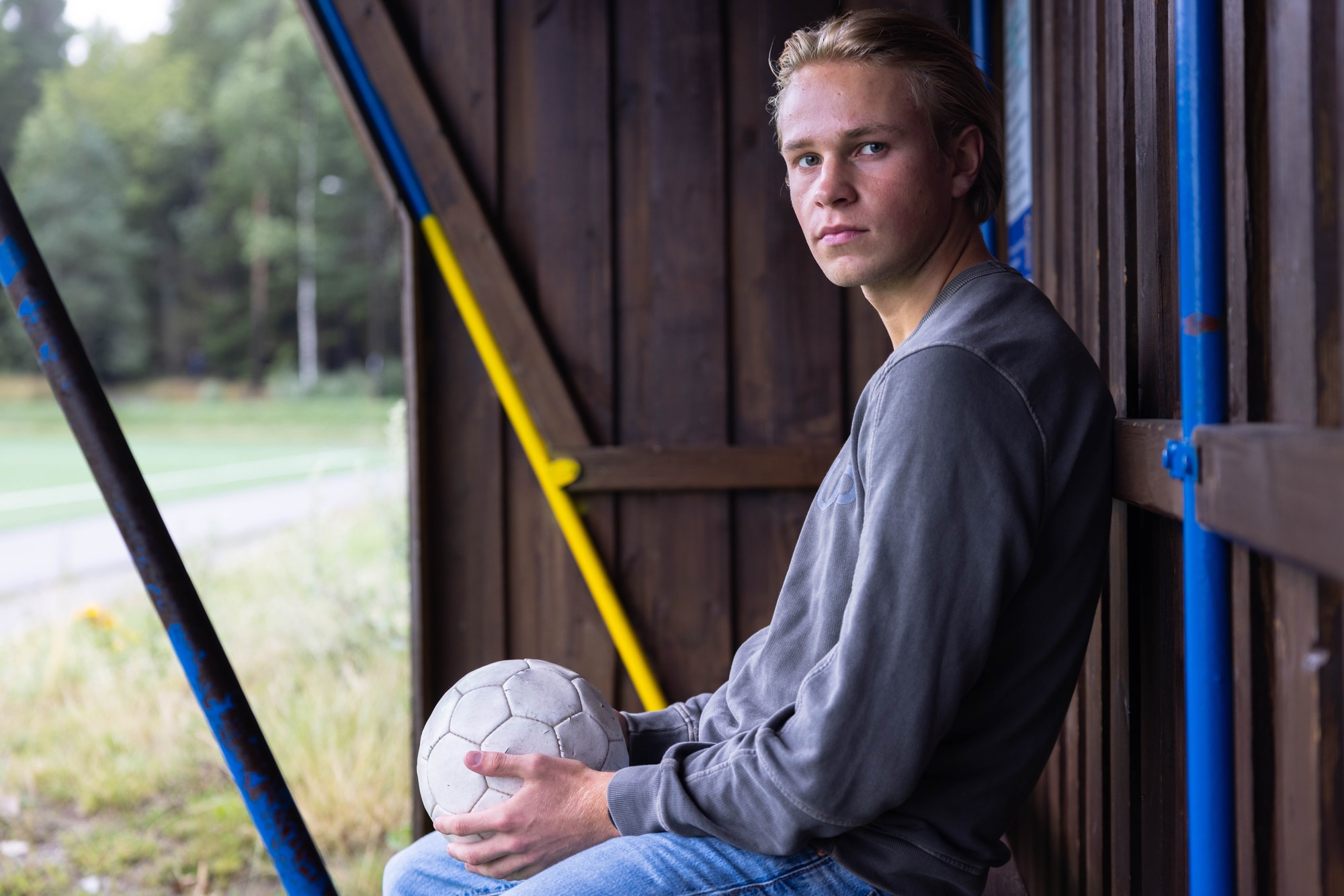 Bilde av Jesper Sandberg som sitter med en ball i hånden på ventebenken ved en fotballbane. 