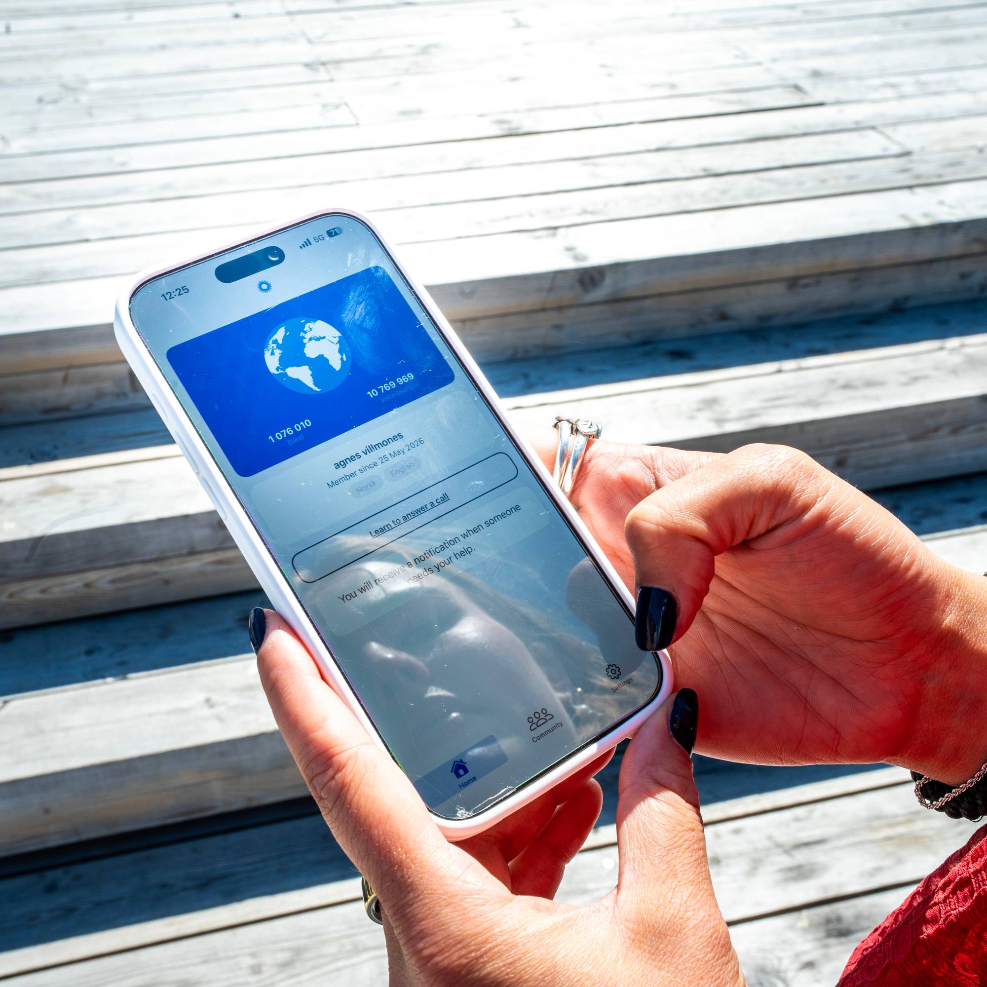 En person holder en mobiltelefon med en applikasjon som viser et verdenskart og brukerprofil. 
