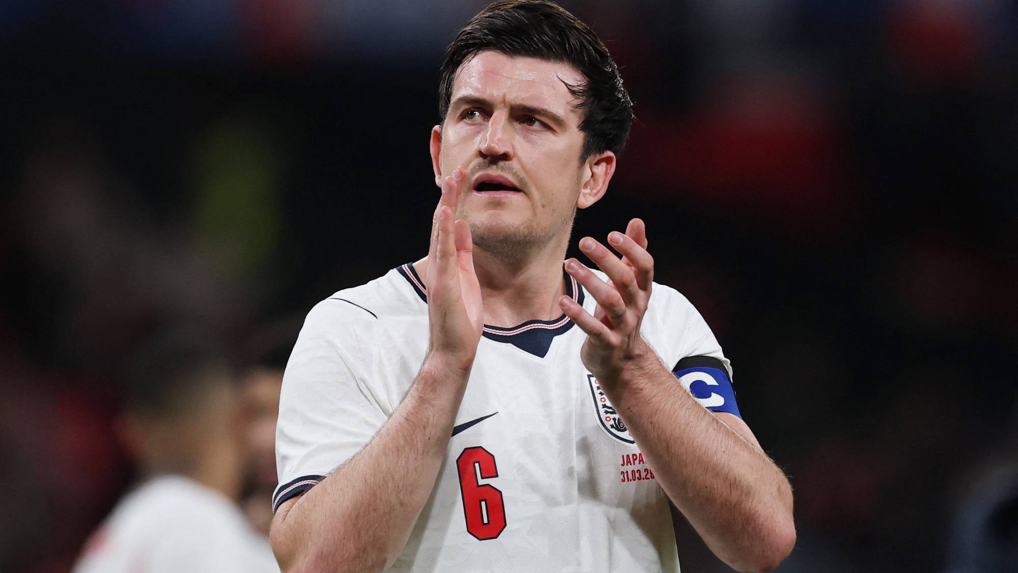 Engelsk fotballspiller Harry Maguire klapper. Han er ikledd den hvite landslagsdrakten med nummer 6 på brystet. Bak ham er publikum. (Bildebeskrivelsen er laget av en KI-tjeneste)