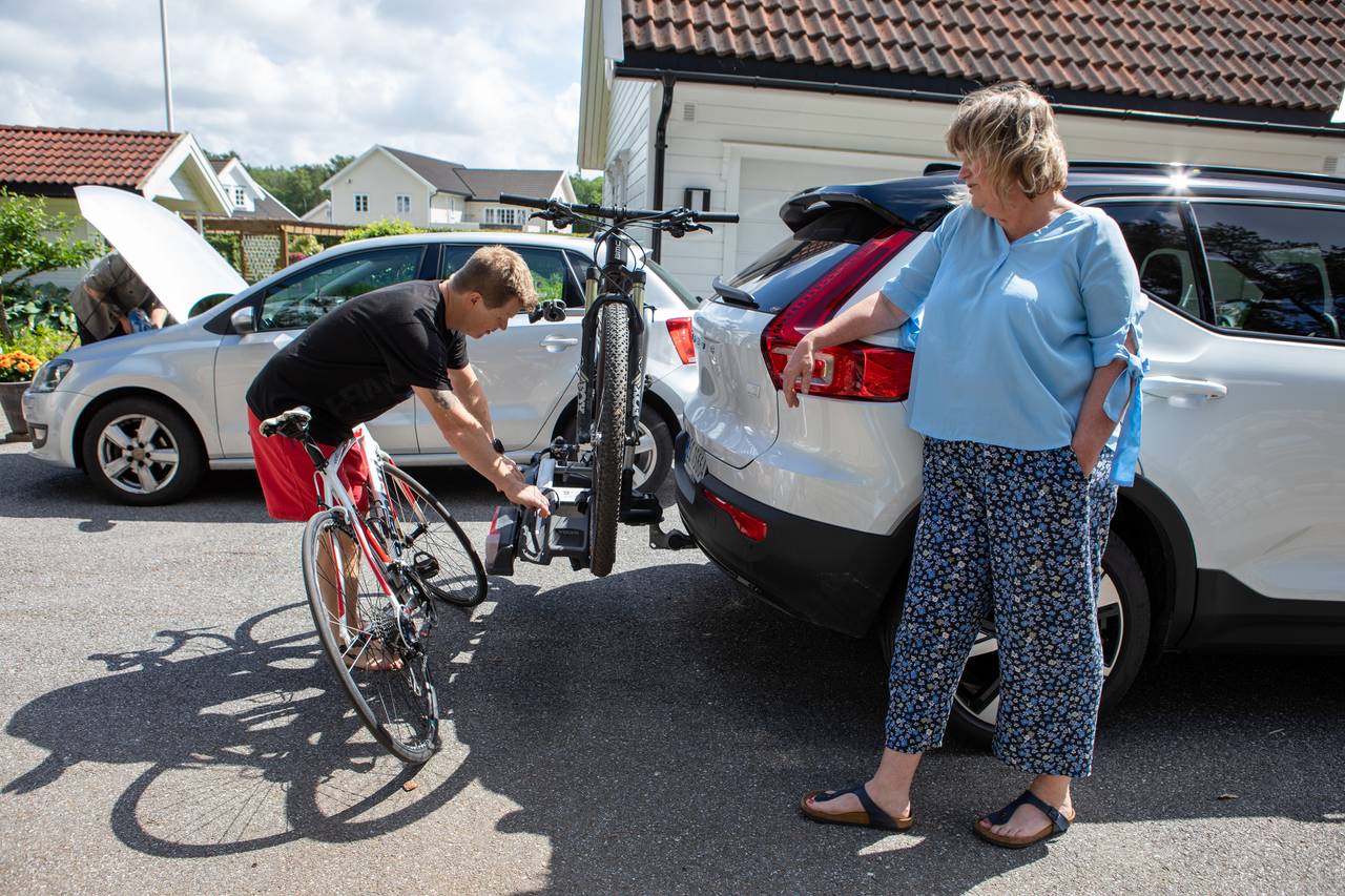 Anne-Grete lener seg på bilen og ser at Trond fester syklene på sykkelstativet.