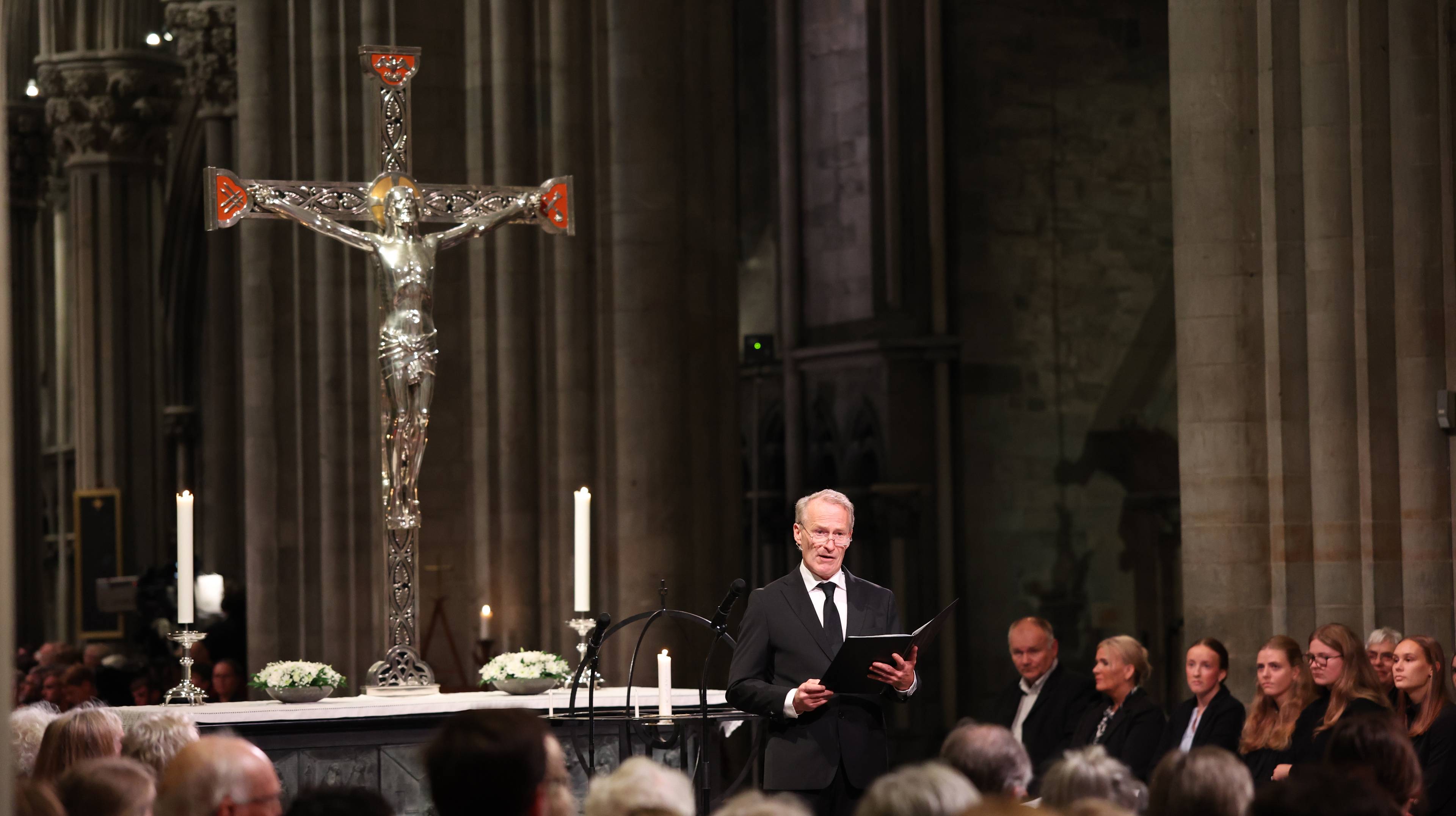 En mann i dress leser fra et hefte foran et alter med krusifiks i Nidarosdomen. (Bildebeskrivelsen er laget av en KI-tjeneste)