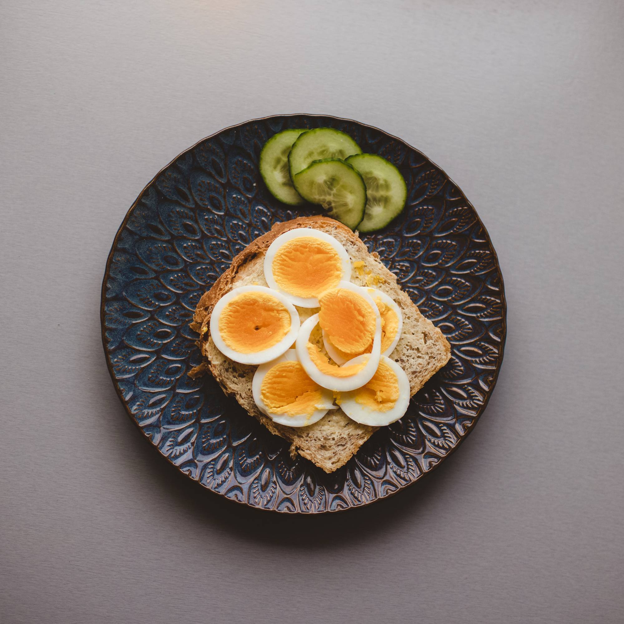 Brødskive med kokt egg og skiver med agurk på en tallerken.