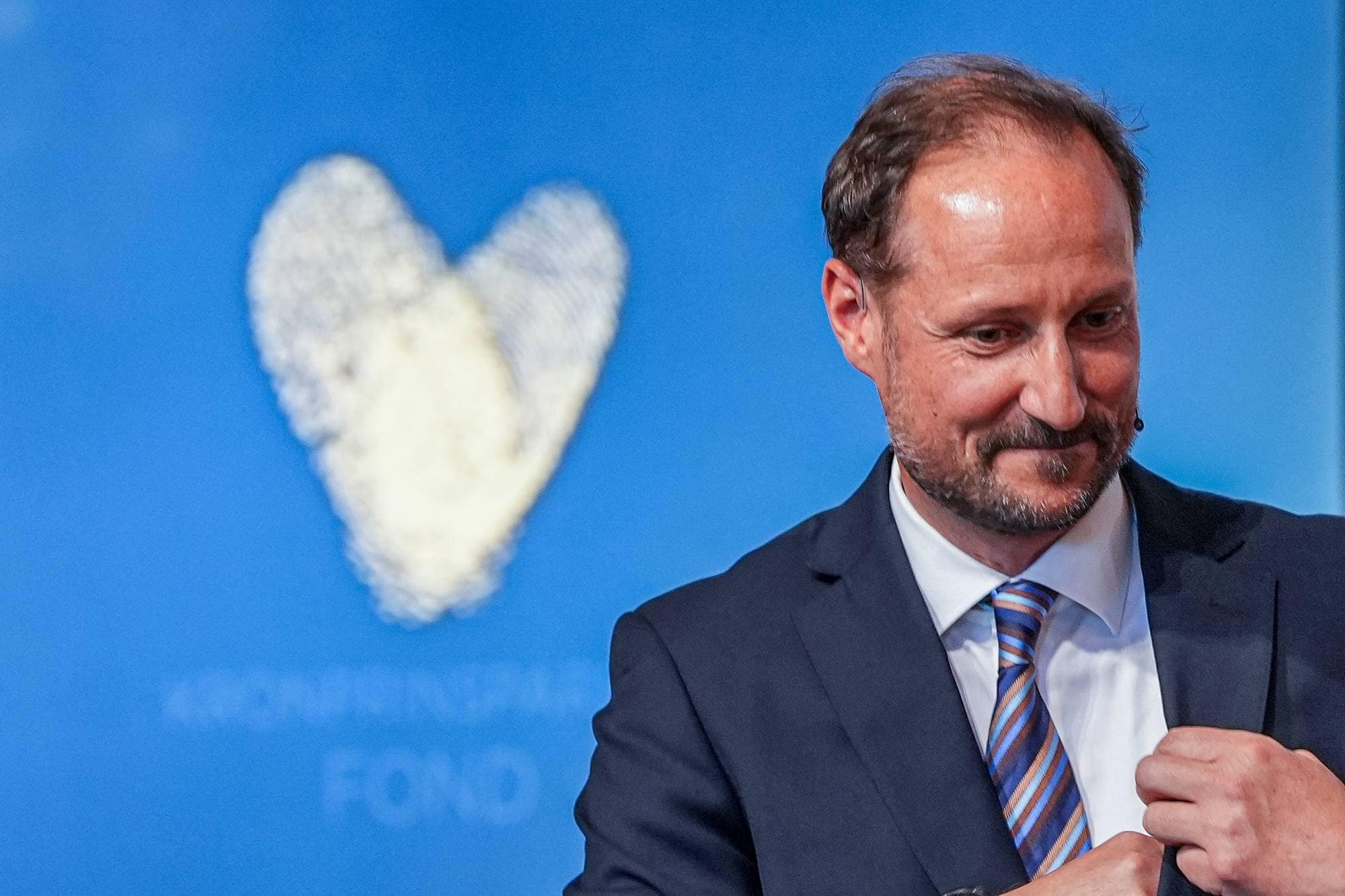 Kronprins Haakon på markeringen av Kronprinsparets fonds 25-årsjubileum på Slottet, han står foran en skjerm der fondets logo, et hjerte, er.